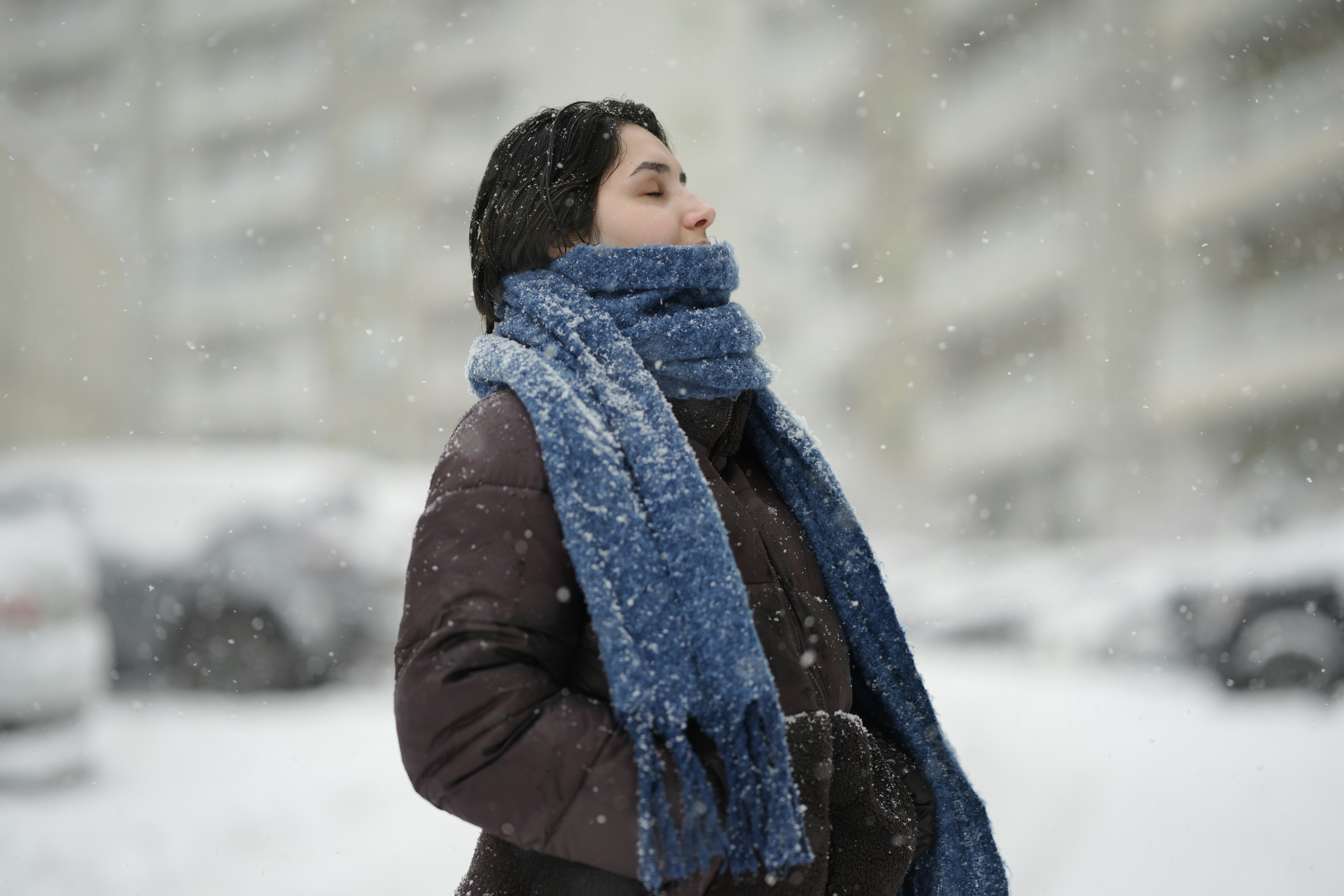 雪の降る中、茶色いジャケットと青いスカーフを身に着けた女性が屋外でいる