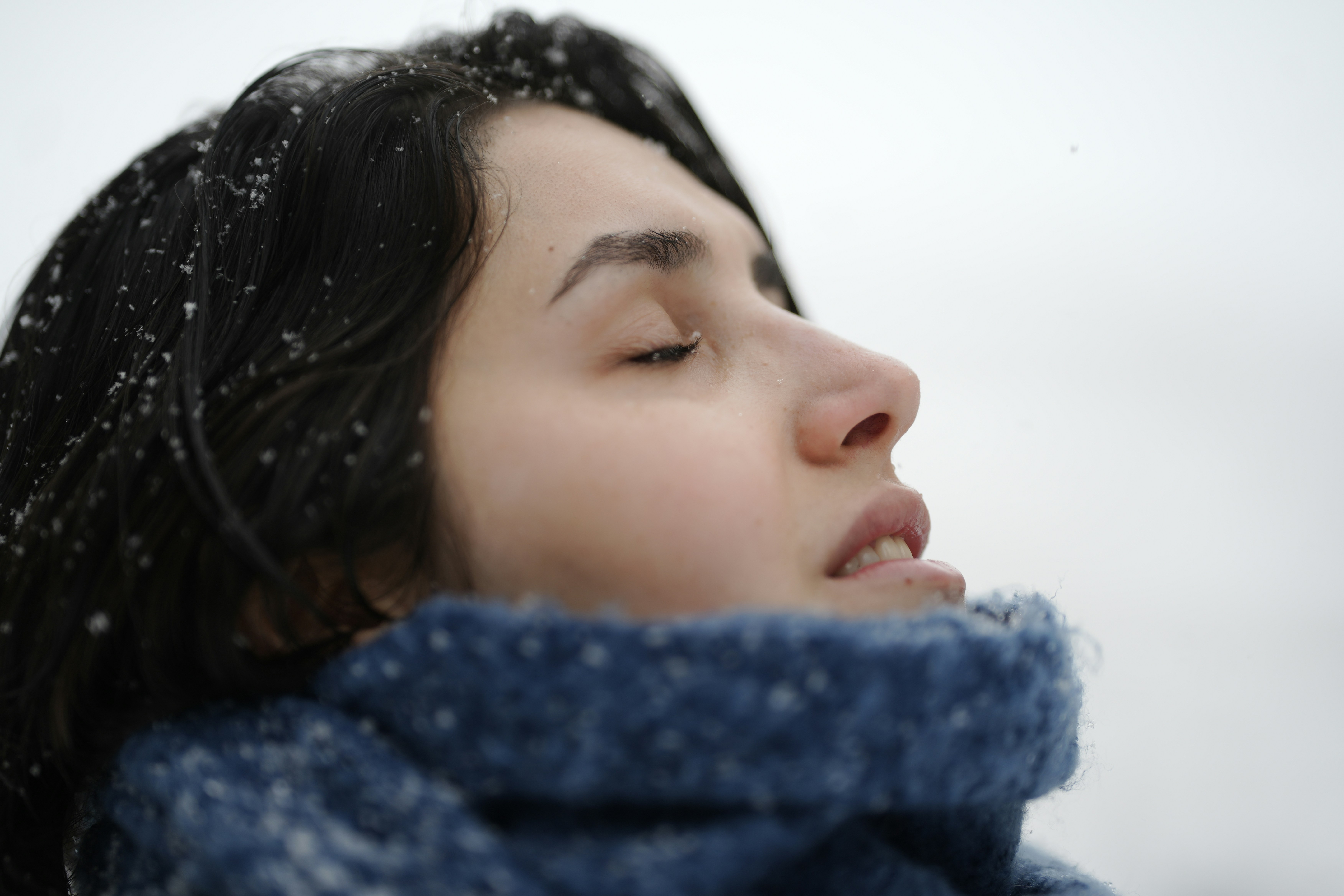 Uma mulher de cabelos escuros e um cachecol azul na neve caindo