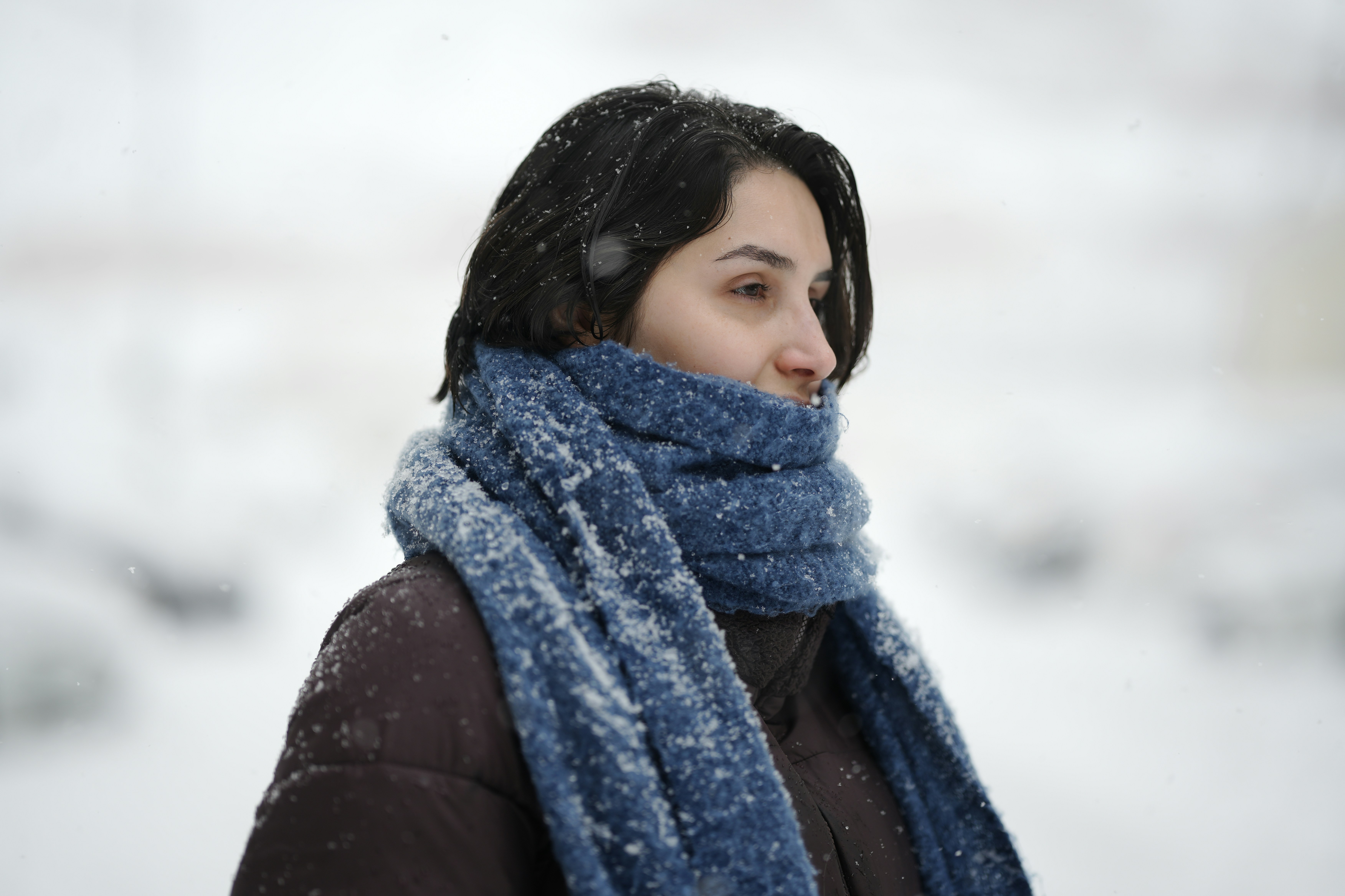 Uma mulher com uma jaqueta marrom escura e cachecol azul coberta de neve clara