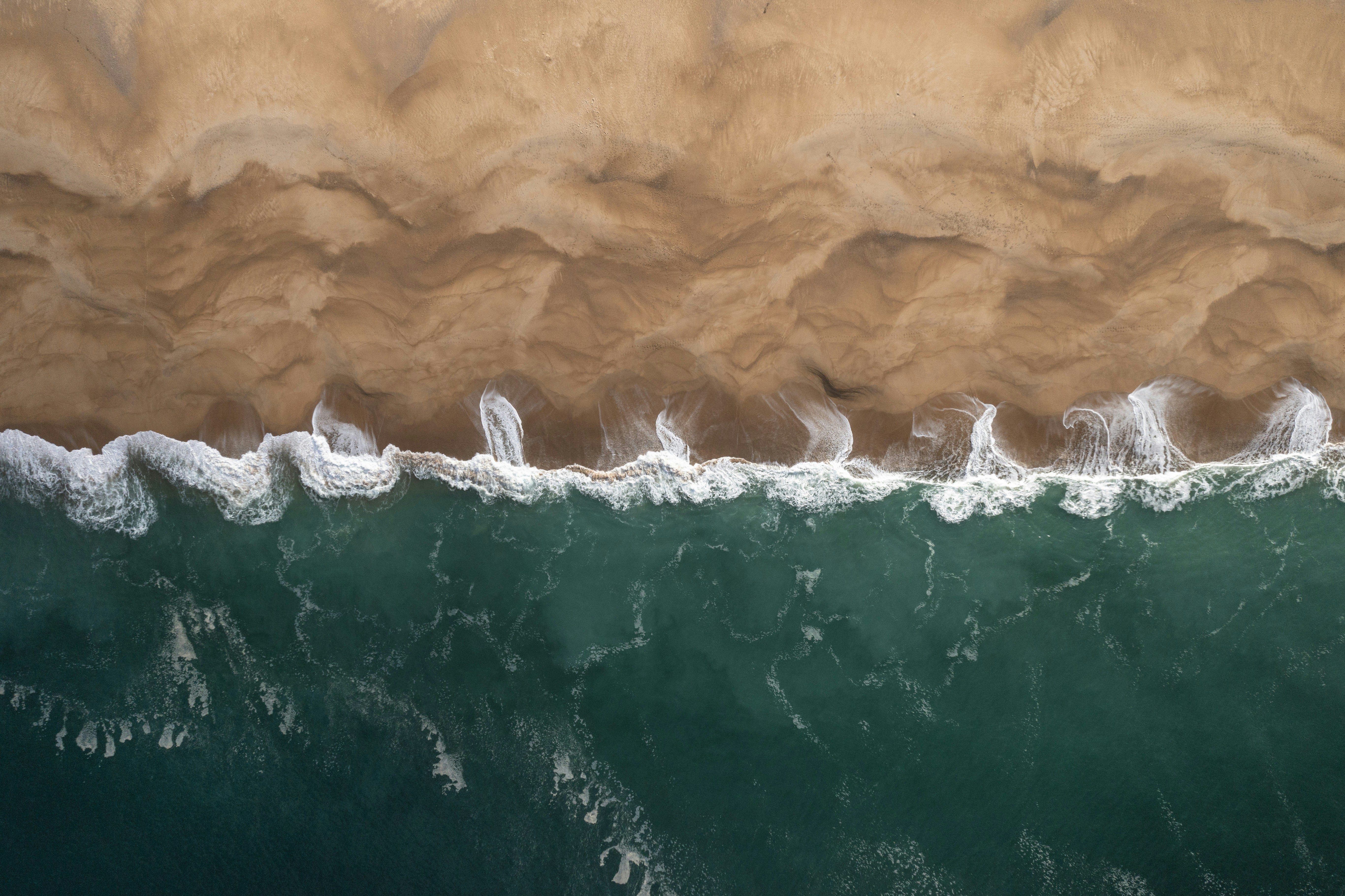Aerial view of turquoise ocean waves crashing onto a sandy beach