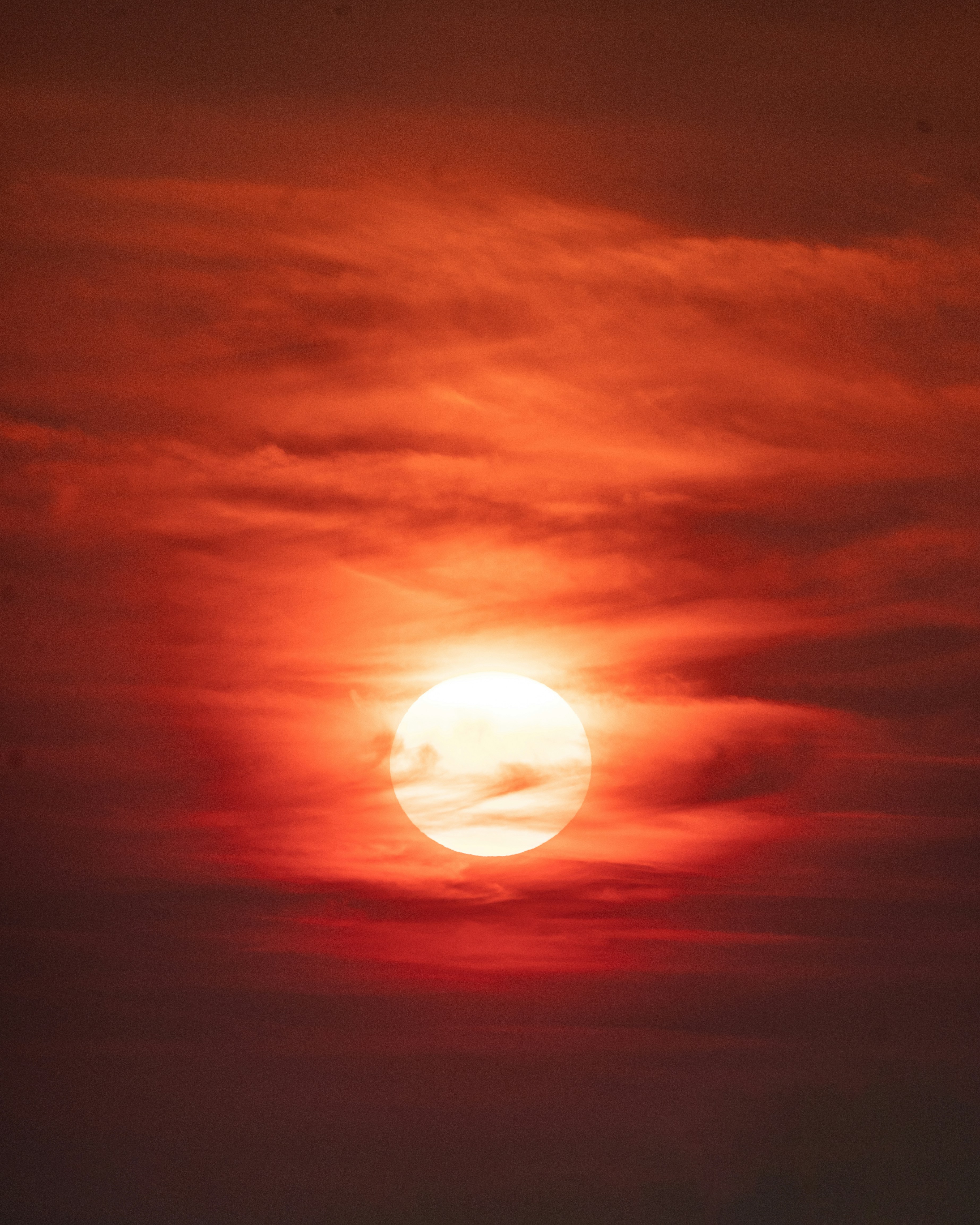 A bright white sun glowing behind a dense layer of vibrant red clouds