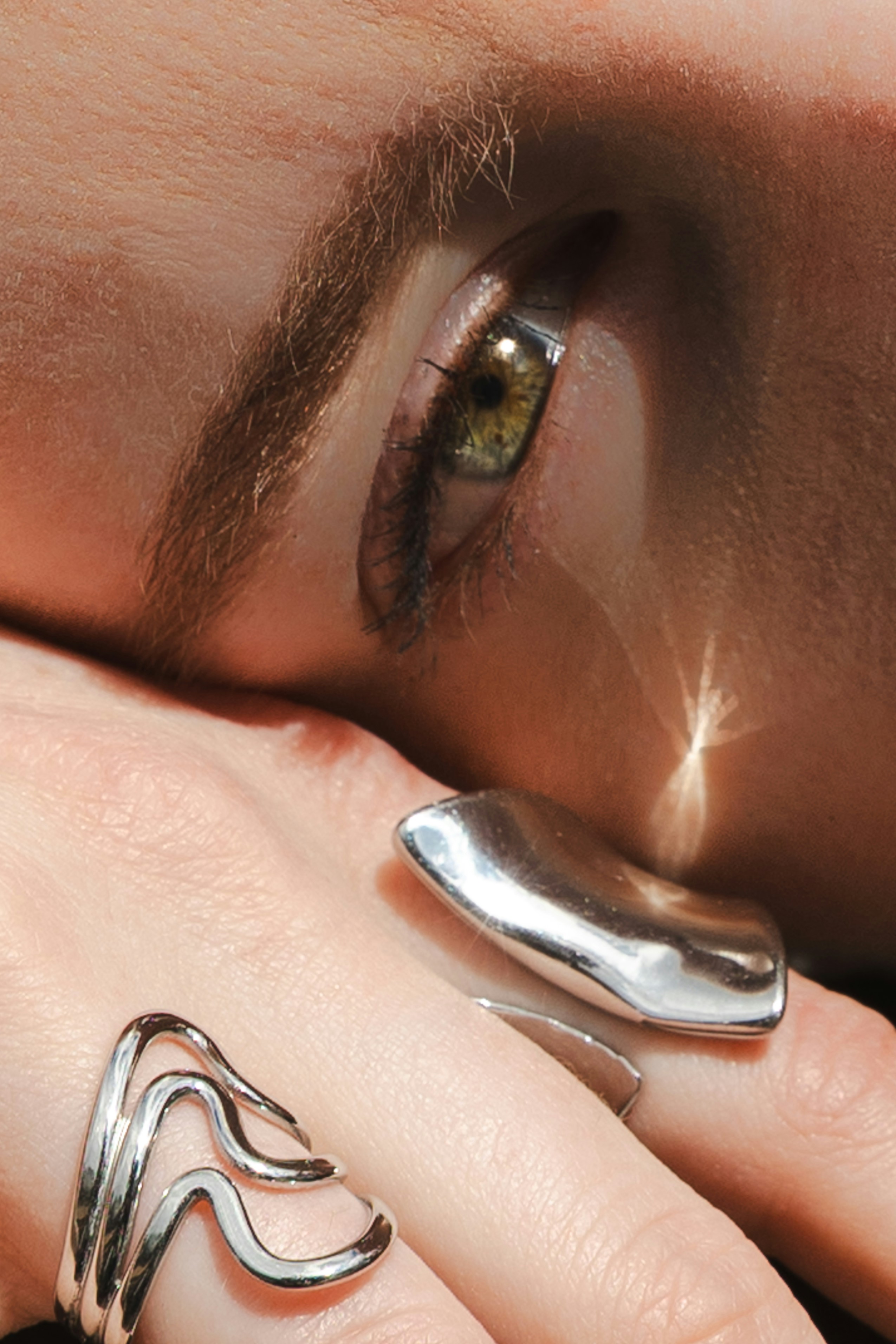 Une personne à l’œil vert posant son visage sur une main portant des bagues en argent