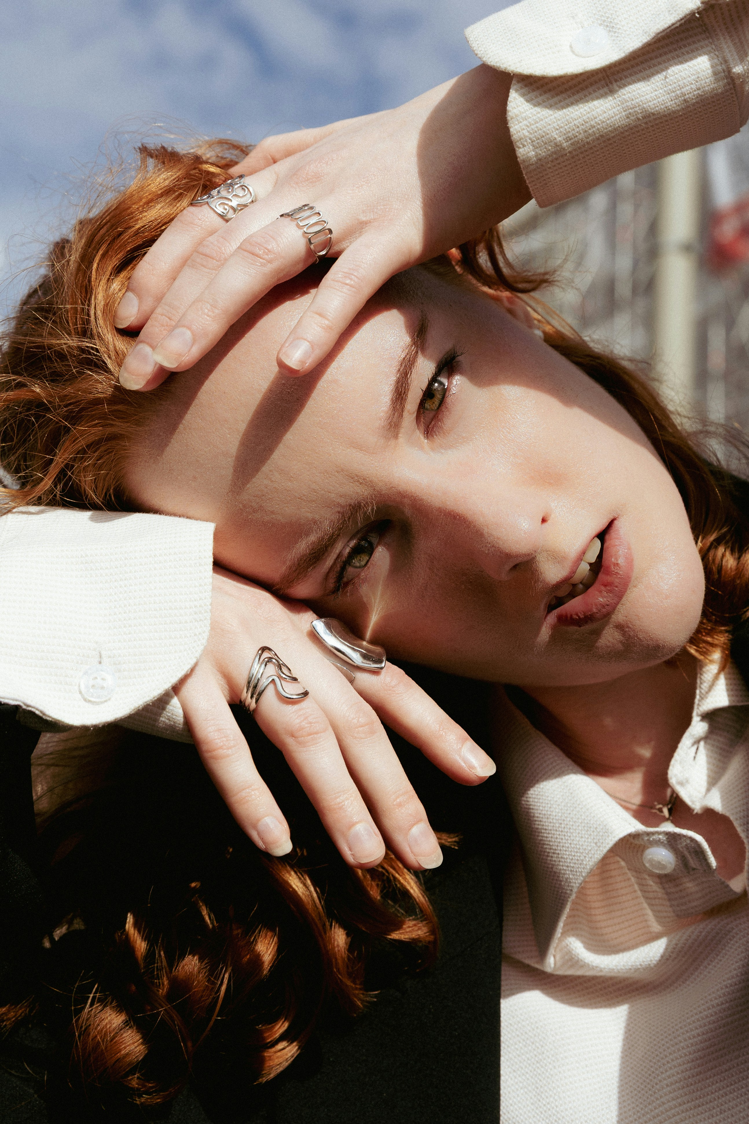 A person with red hair wearing silver rings on their fingers in sunlight