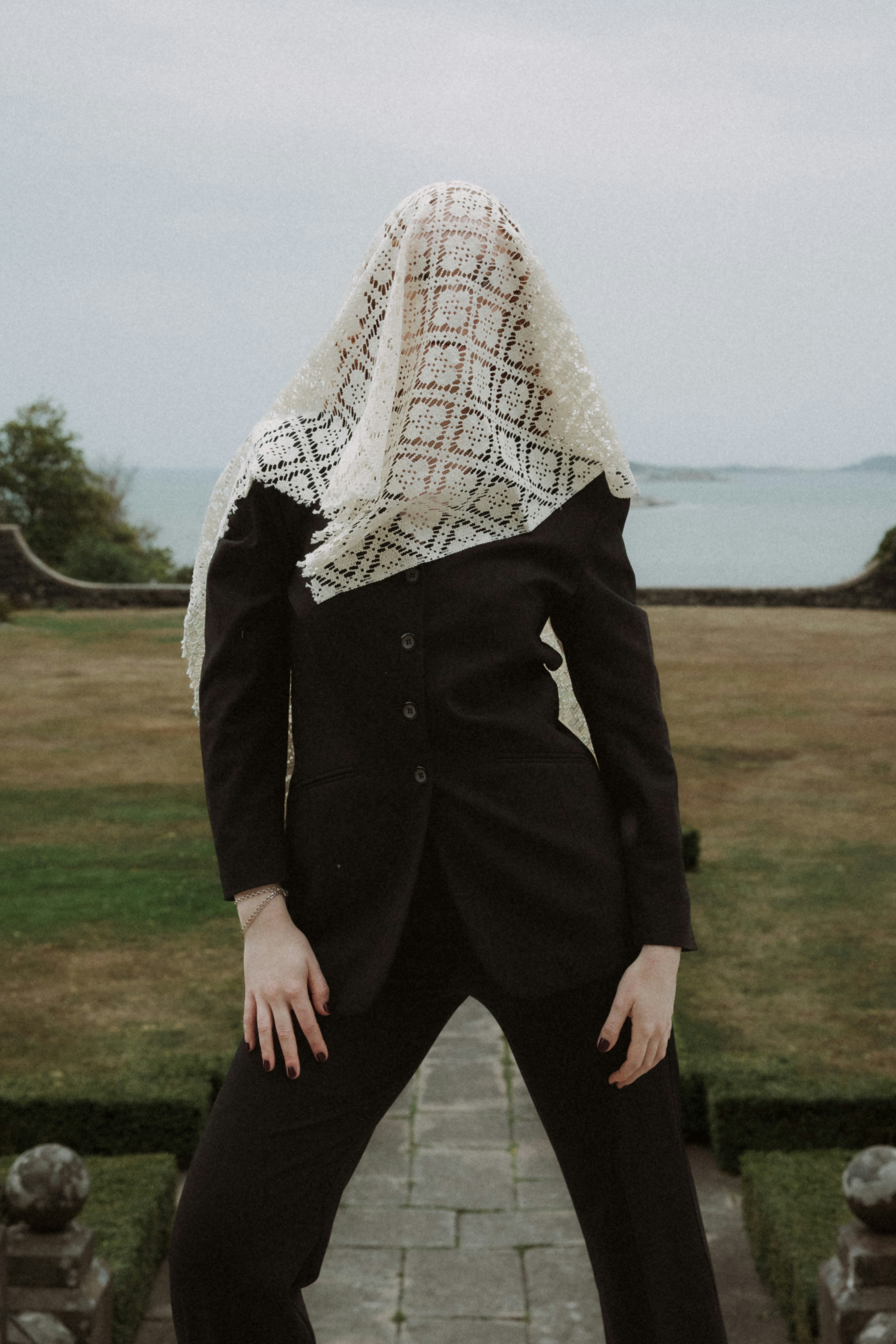 A person in a black suit with a lace veil over their face