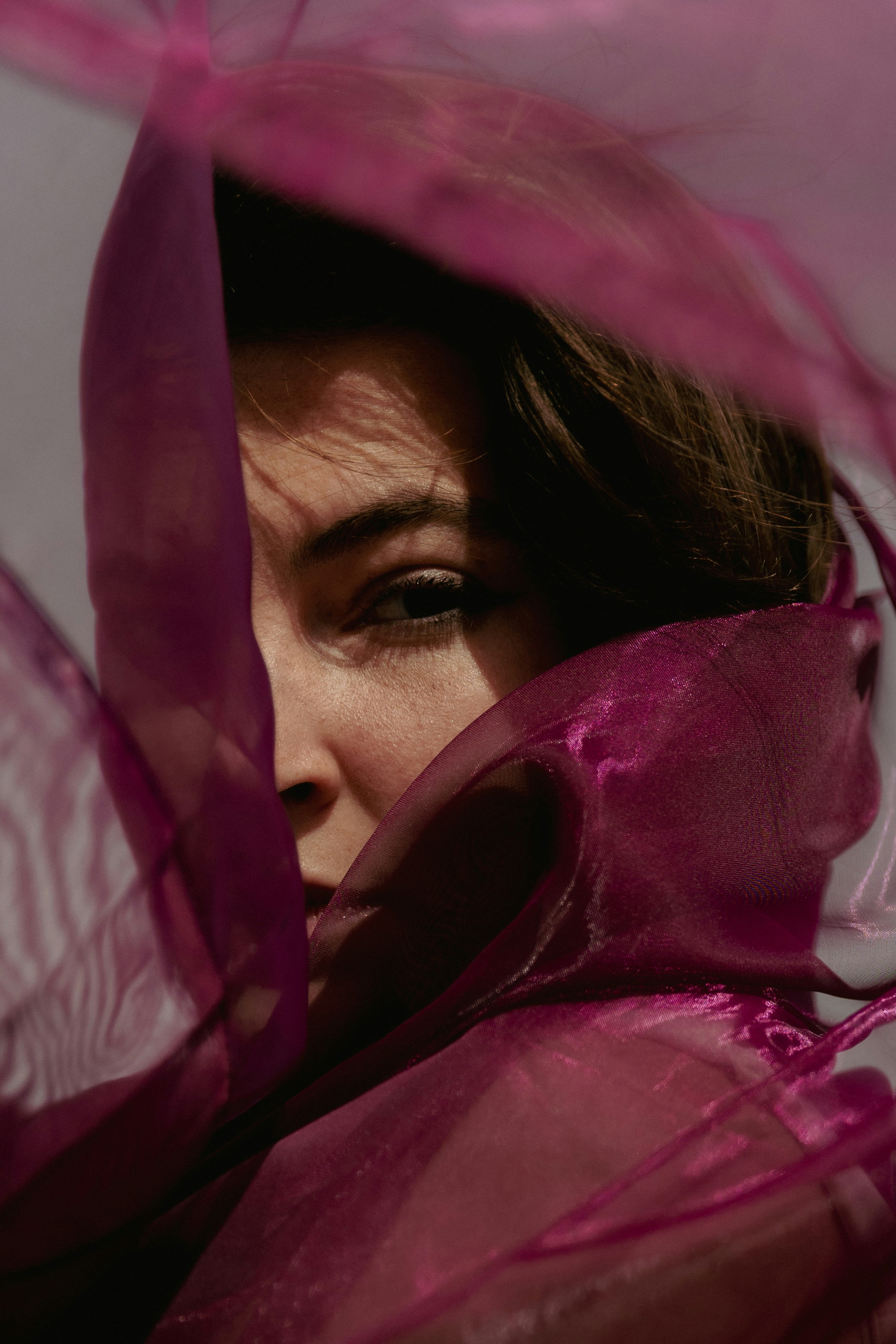 Une personne aux cheveux foncés partiellement cachés par un tissu violet transparent