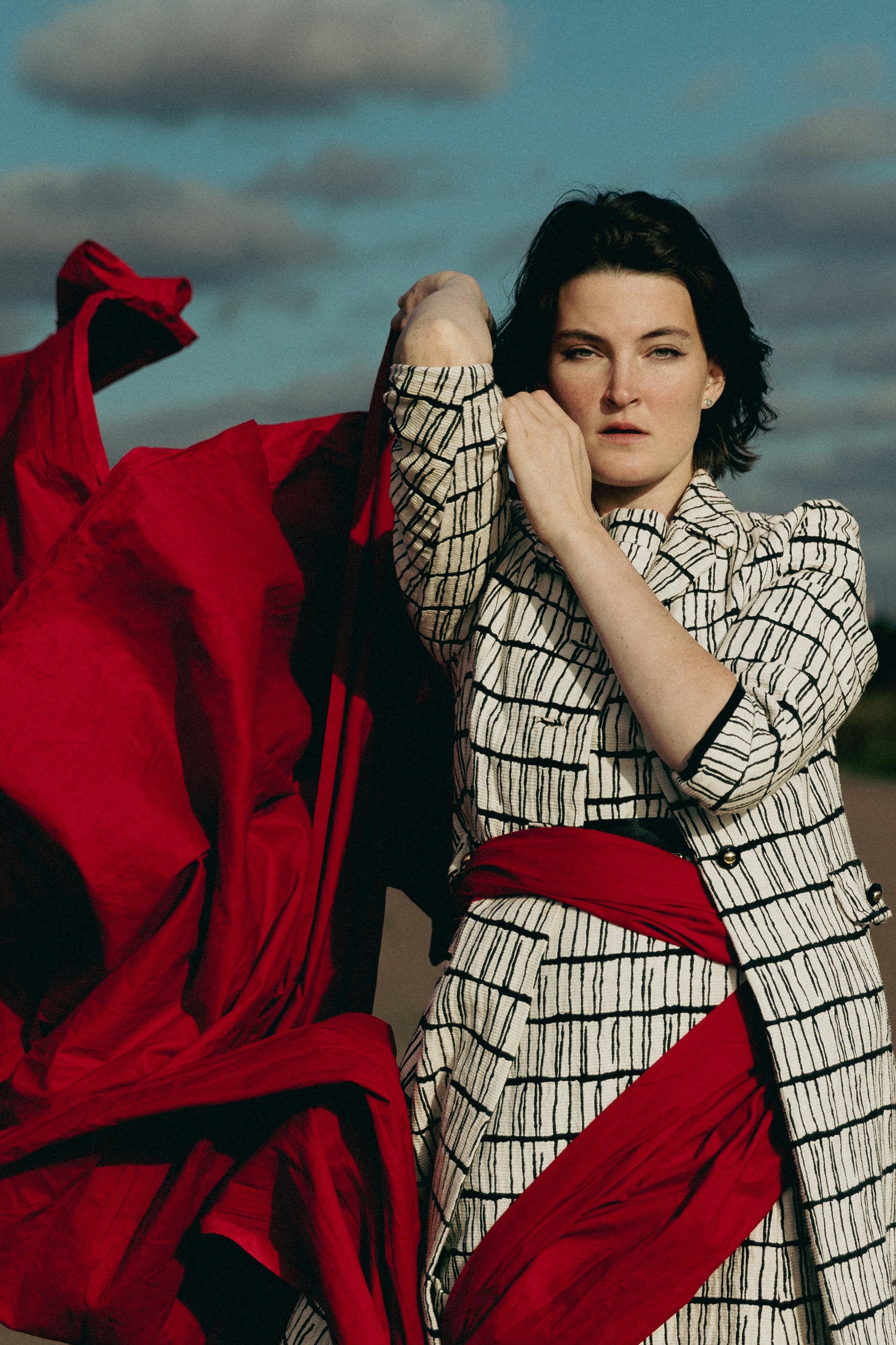 Une femme en manteau noir et blanc tenant un tissu rouge fluide