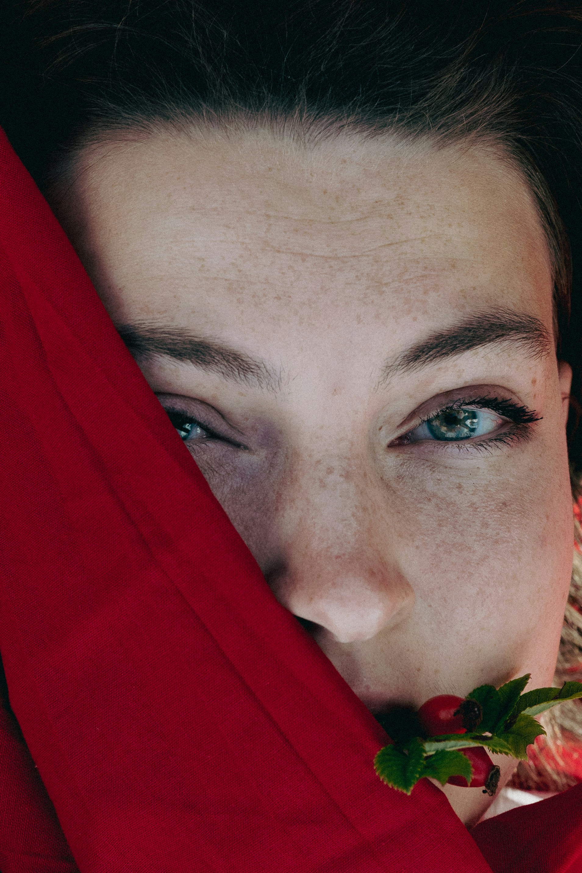 Une personne aux taches de rousseur et aux yeux bleus partiellement cachés par un tissu rouge