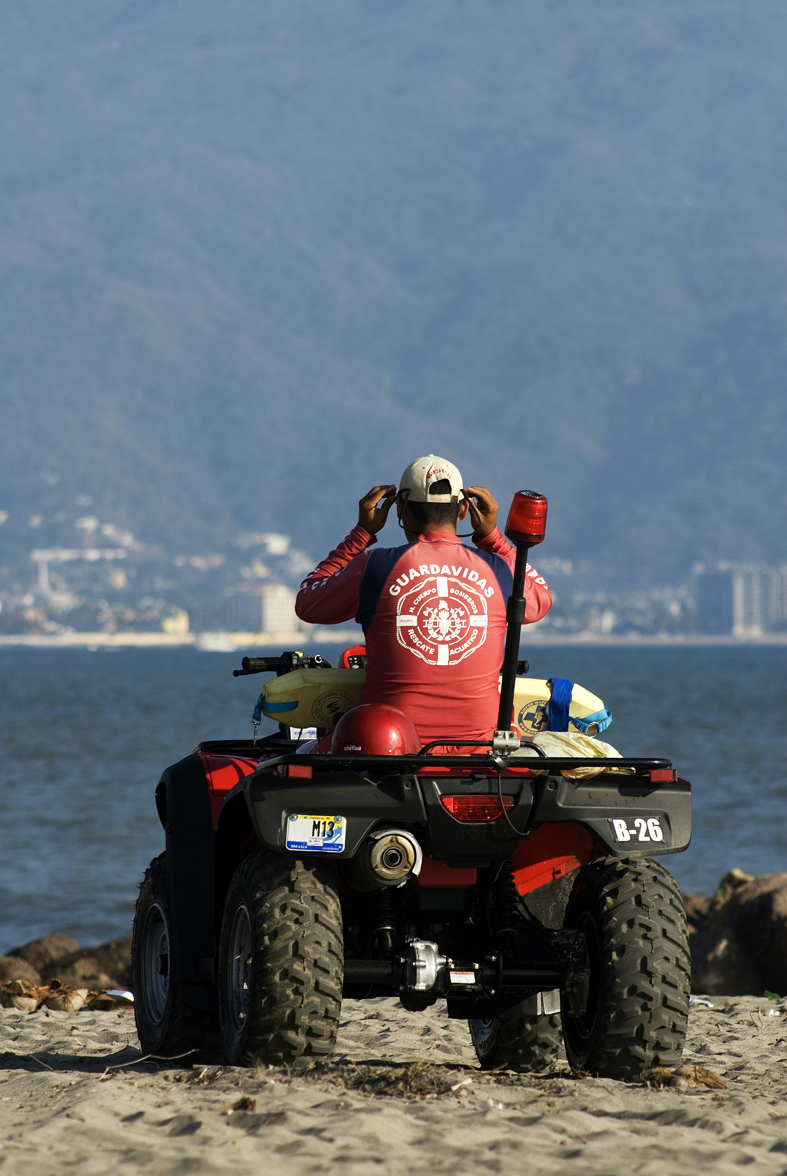 A lifeguard in a red shirt on an ATV on a sandy beach