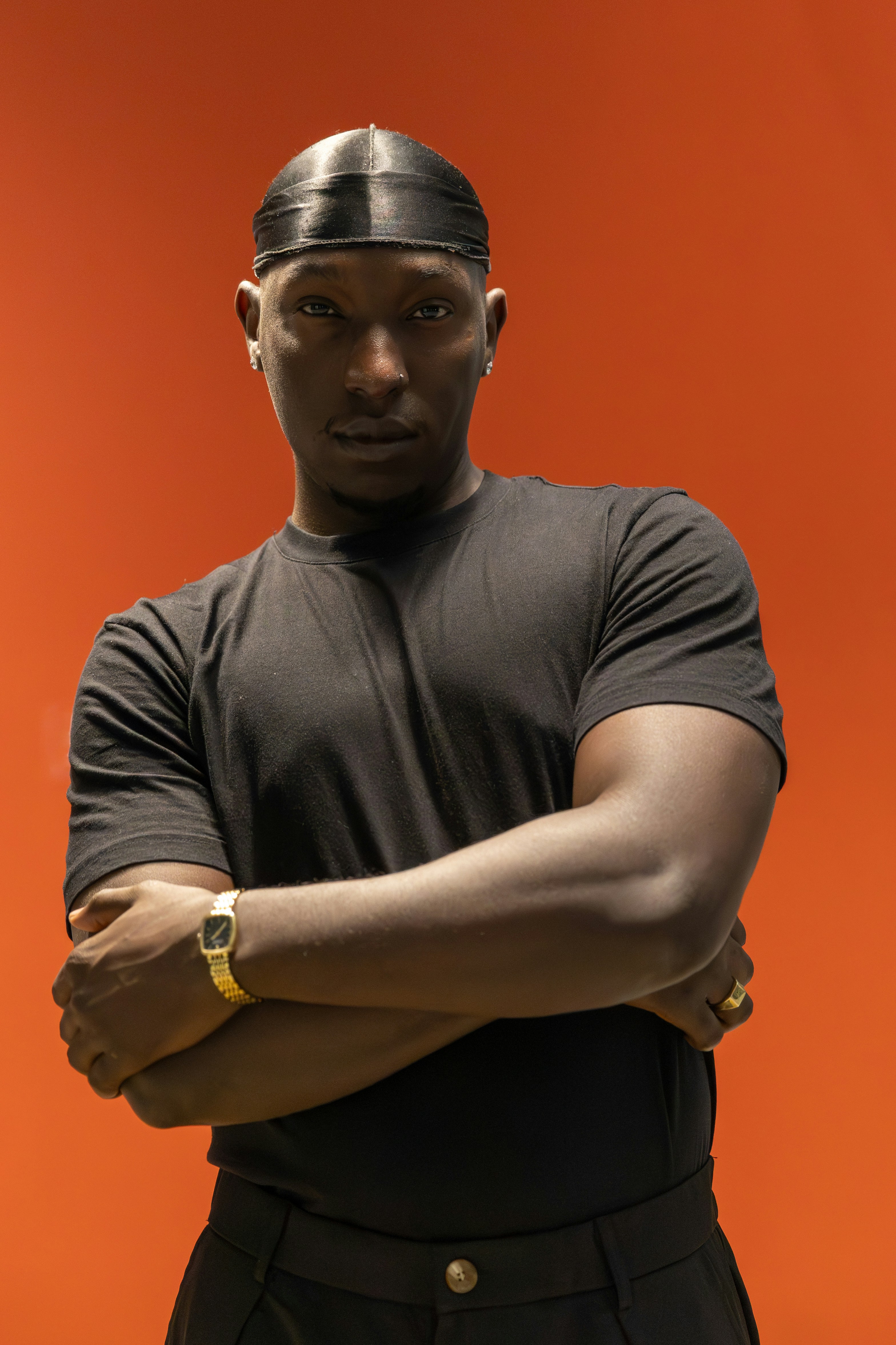 Un homme en t-shirt noir et durag sur fond orange uni