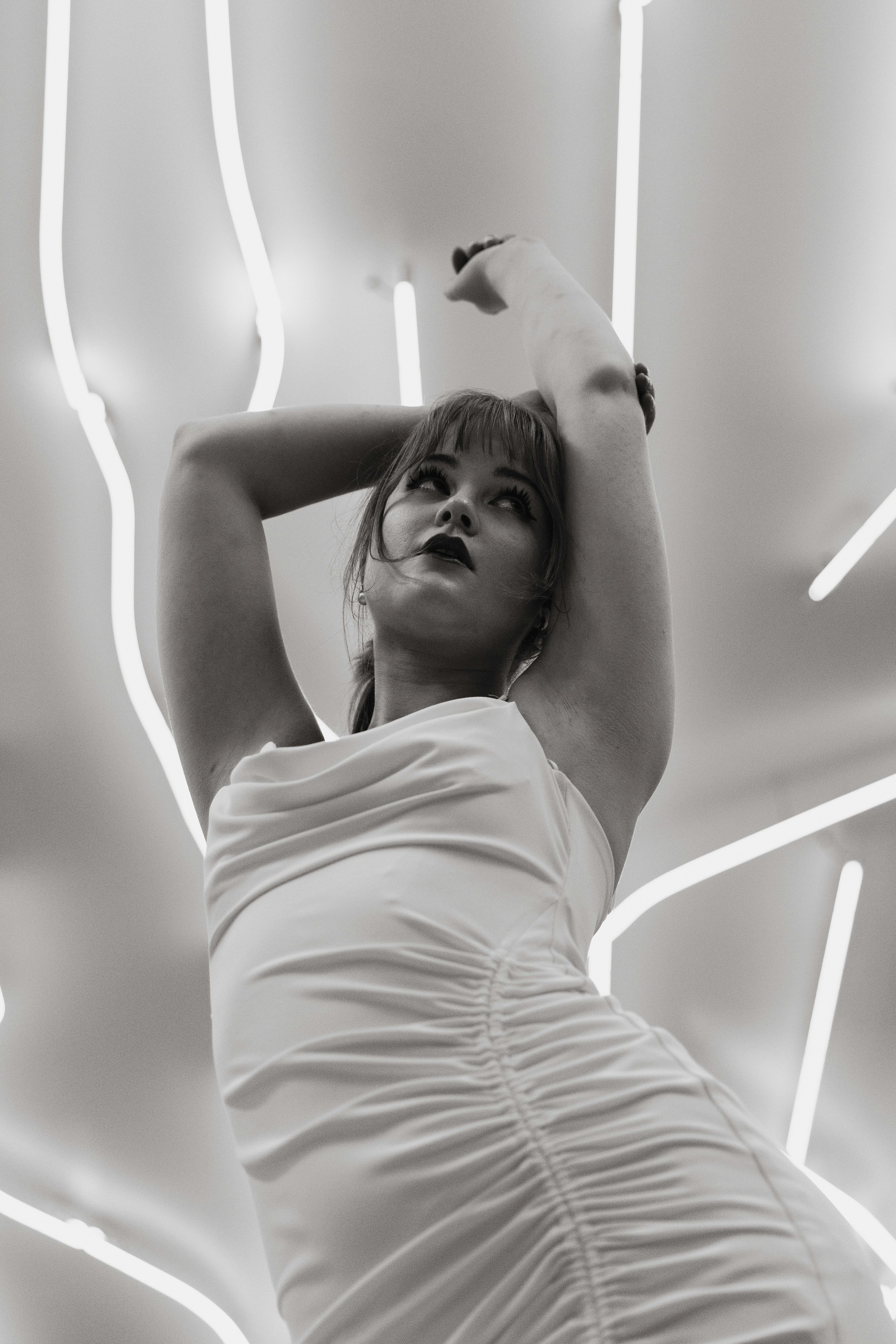 Une femme en robe blanche posant sur un fond de tubes néon lumineux