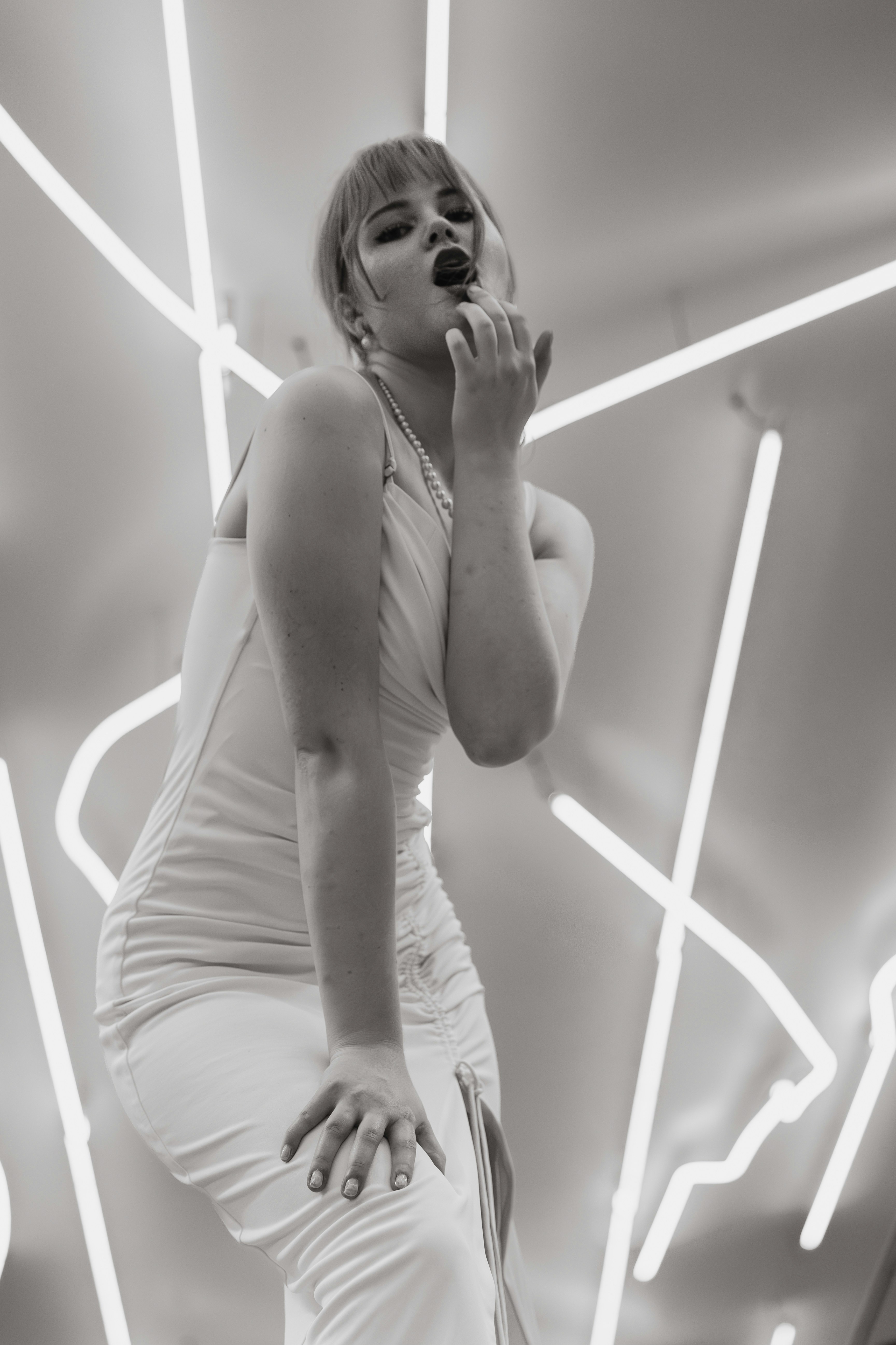 Une femme en robe blanche et collier de perles contre des tubes lumineux lumineux