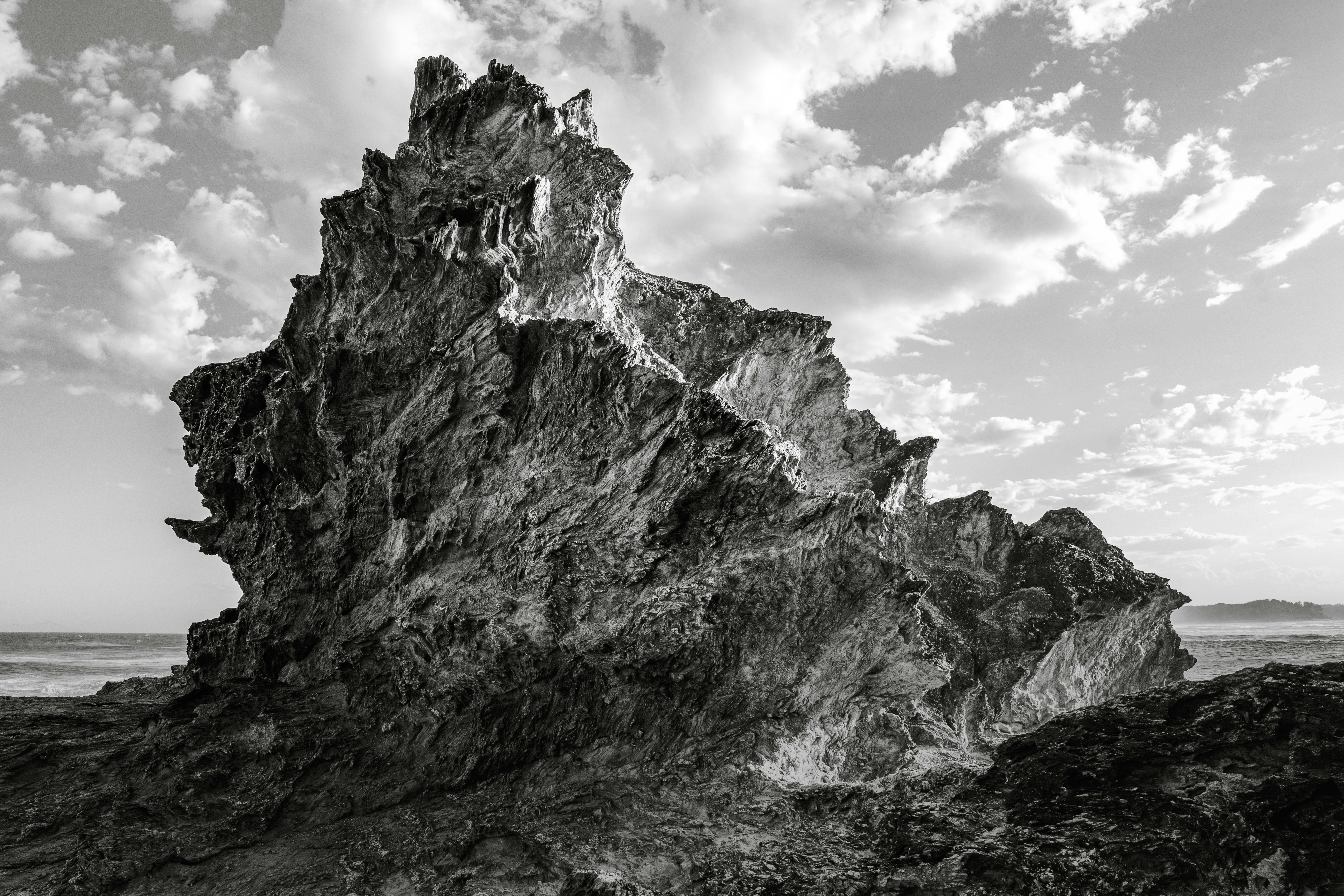 A jagged rock formation on a coastline under a cloudy sky in black and white