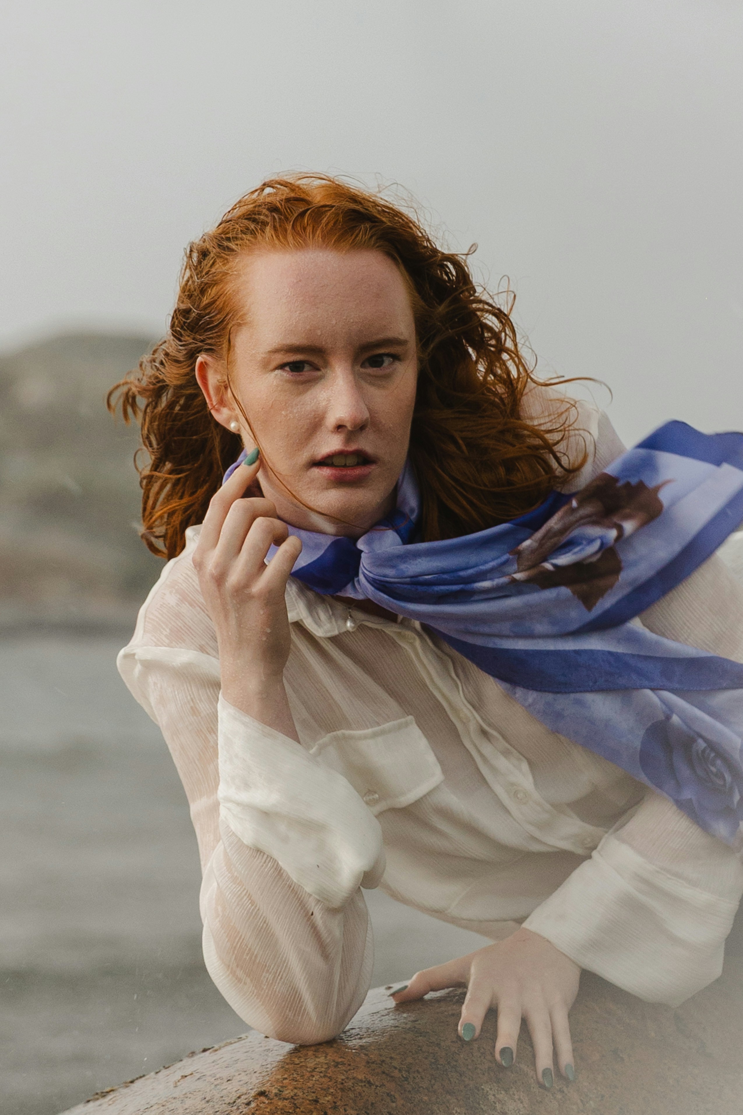 Une femme aux cheveux roux portant une chemise blanche et une écharpe bleue à l’extérieur