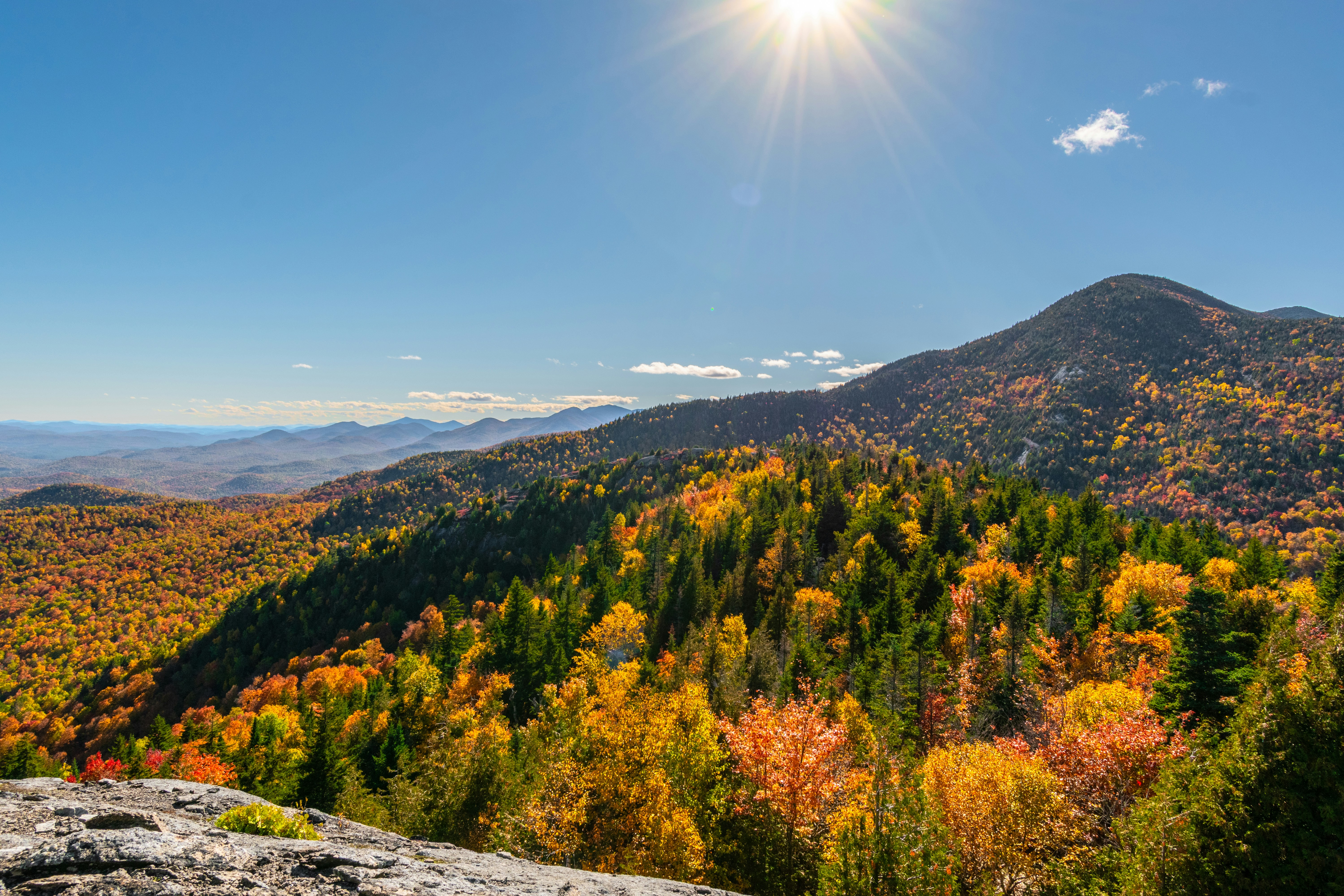 A vast mountain landscape with autumn foliage under a bright sun in a blue sky
