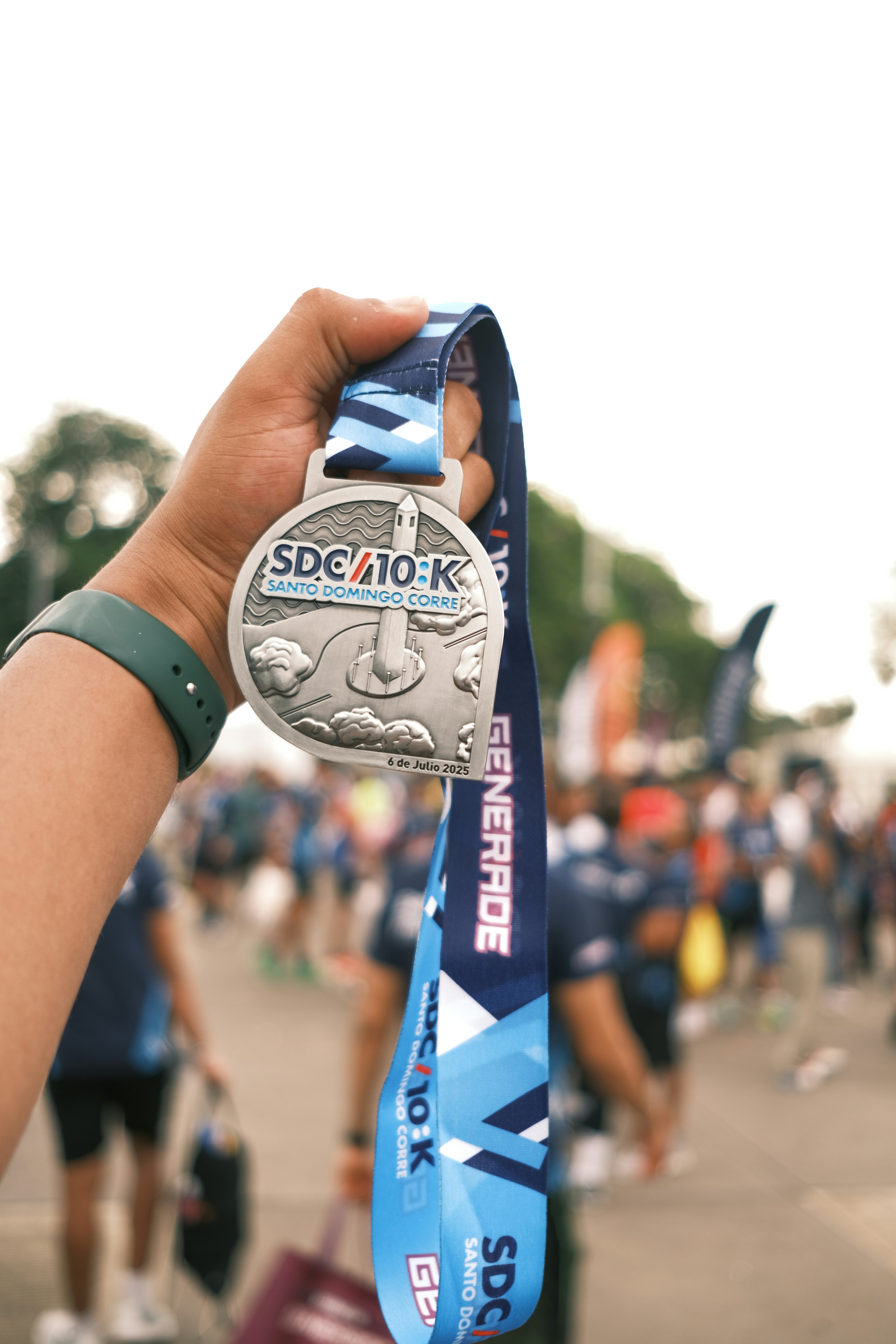 A hand holding a silver race medal with a blue lanyard at a marathon