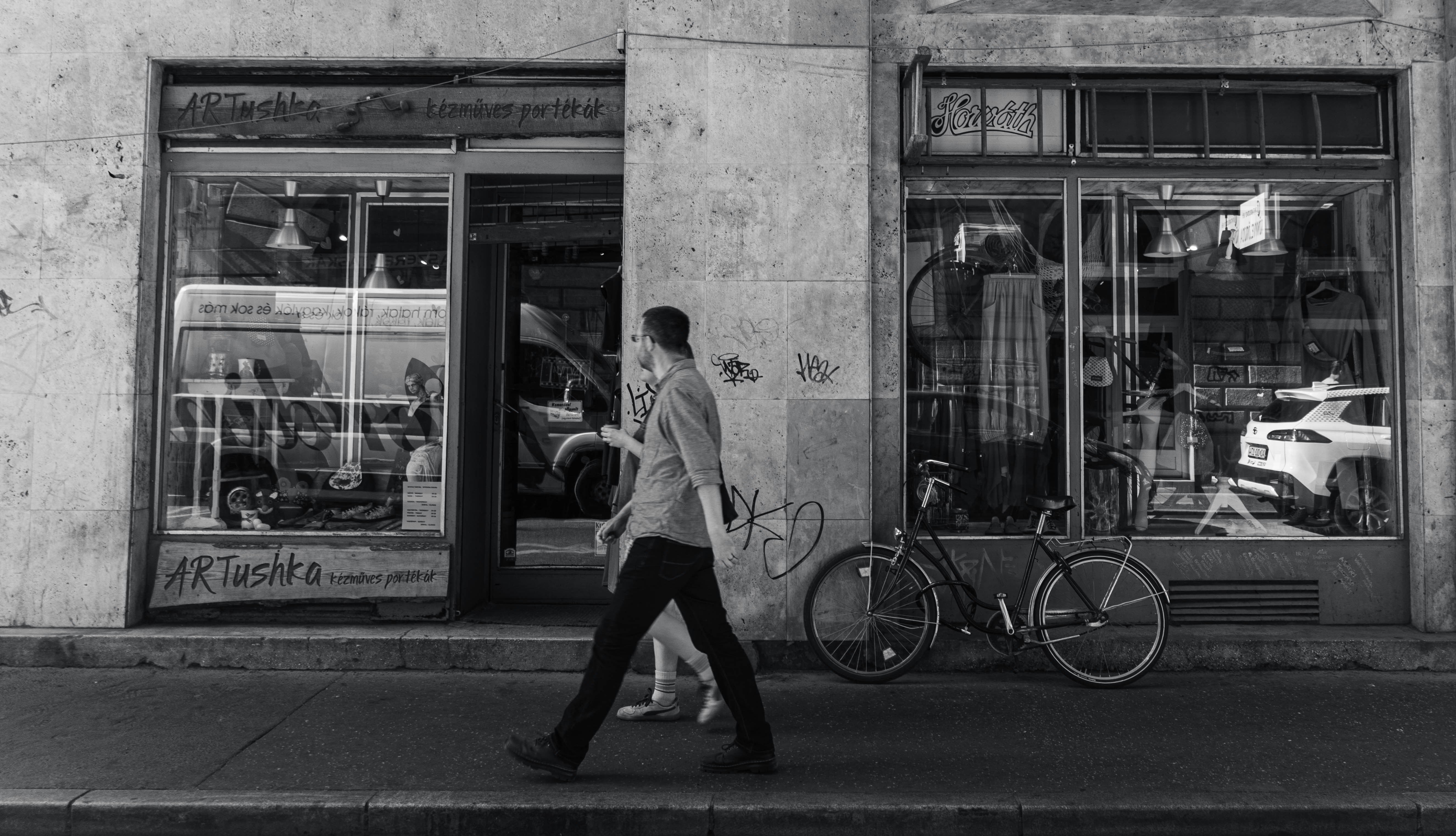 A person walking past shopfronts with a bicycle parked on the sidewalk
