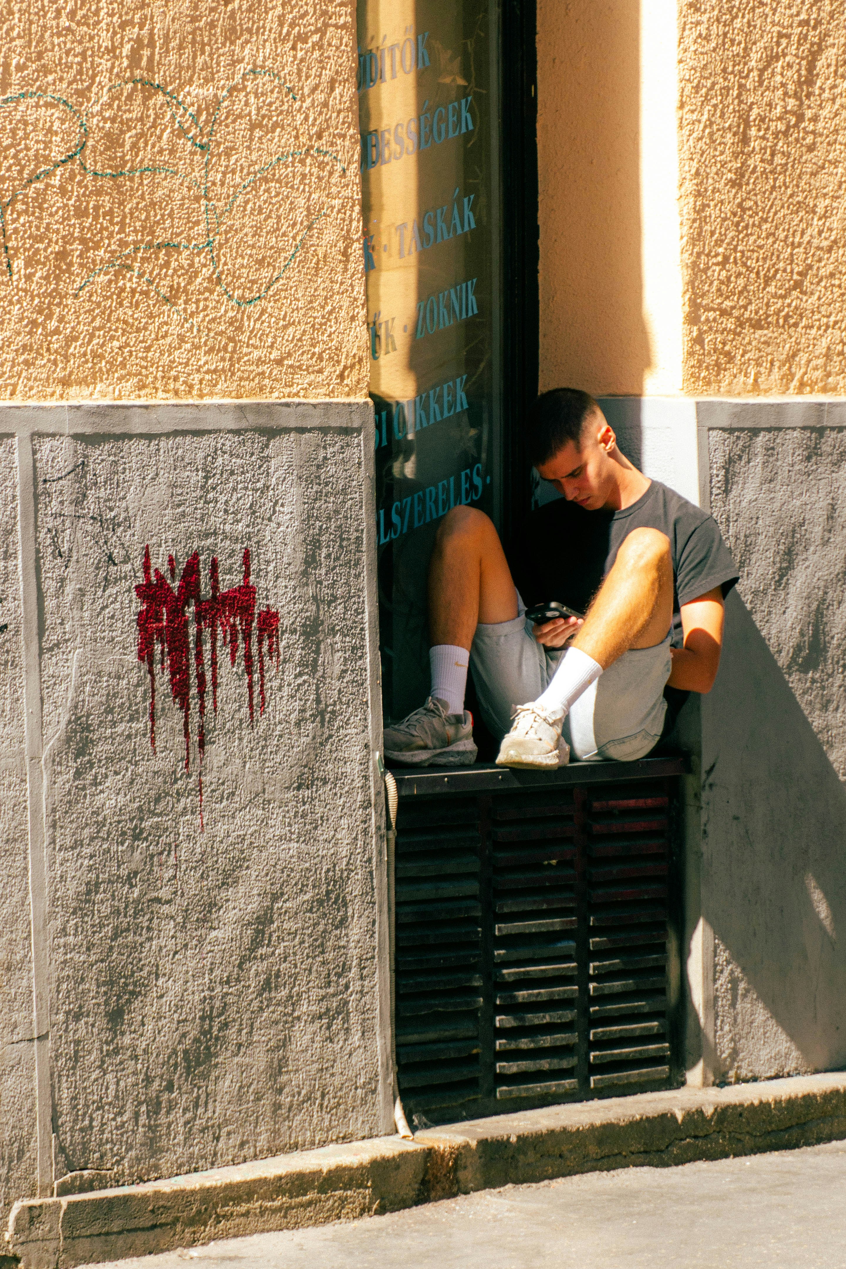 A young man in a black t-shirt and shorts using a phone on a ledge