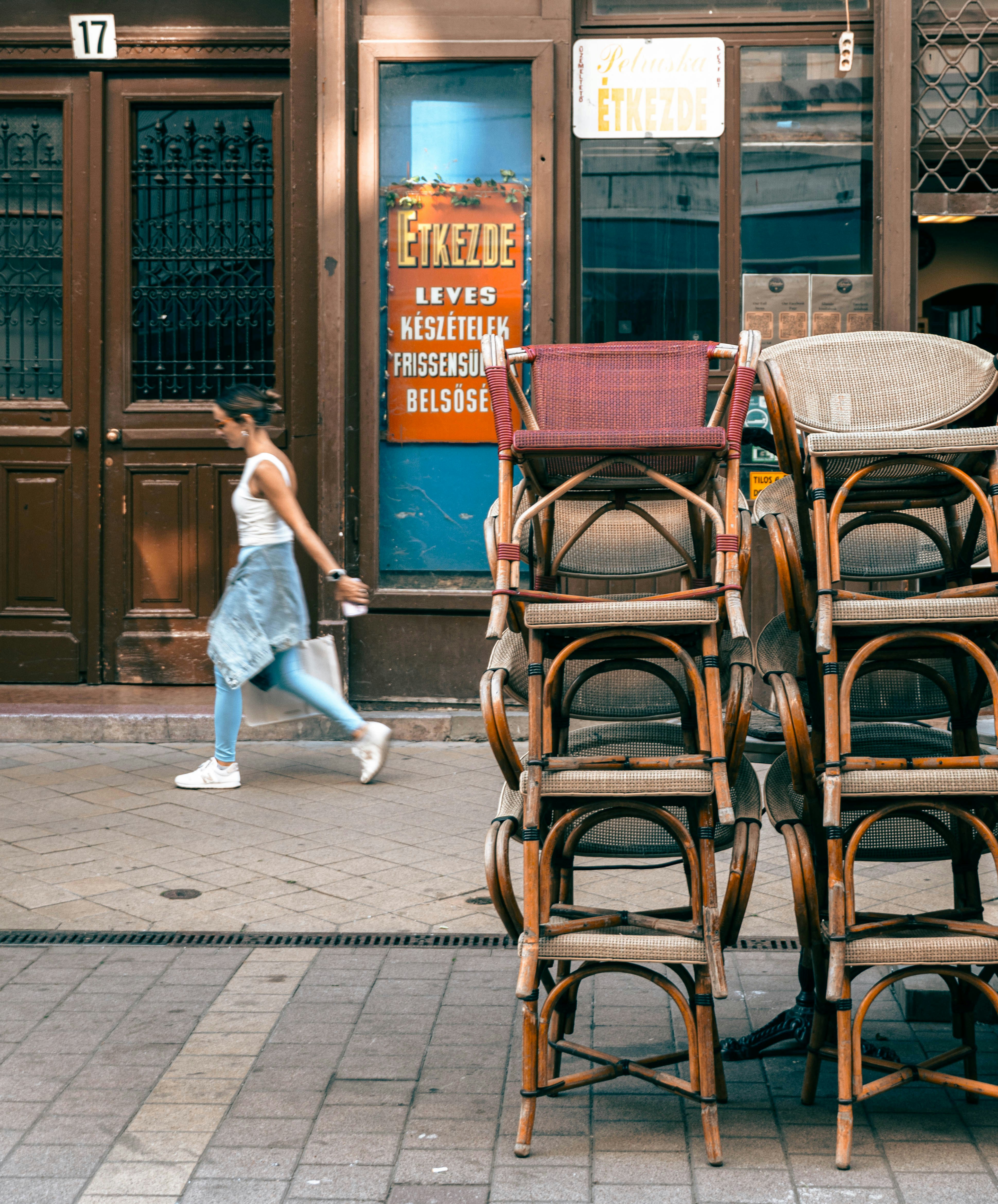 A woman walking past stacked chairs outside a restaurant with an orange sign