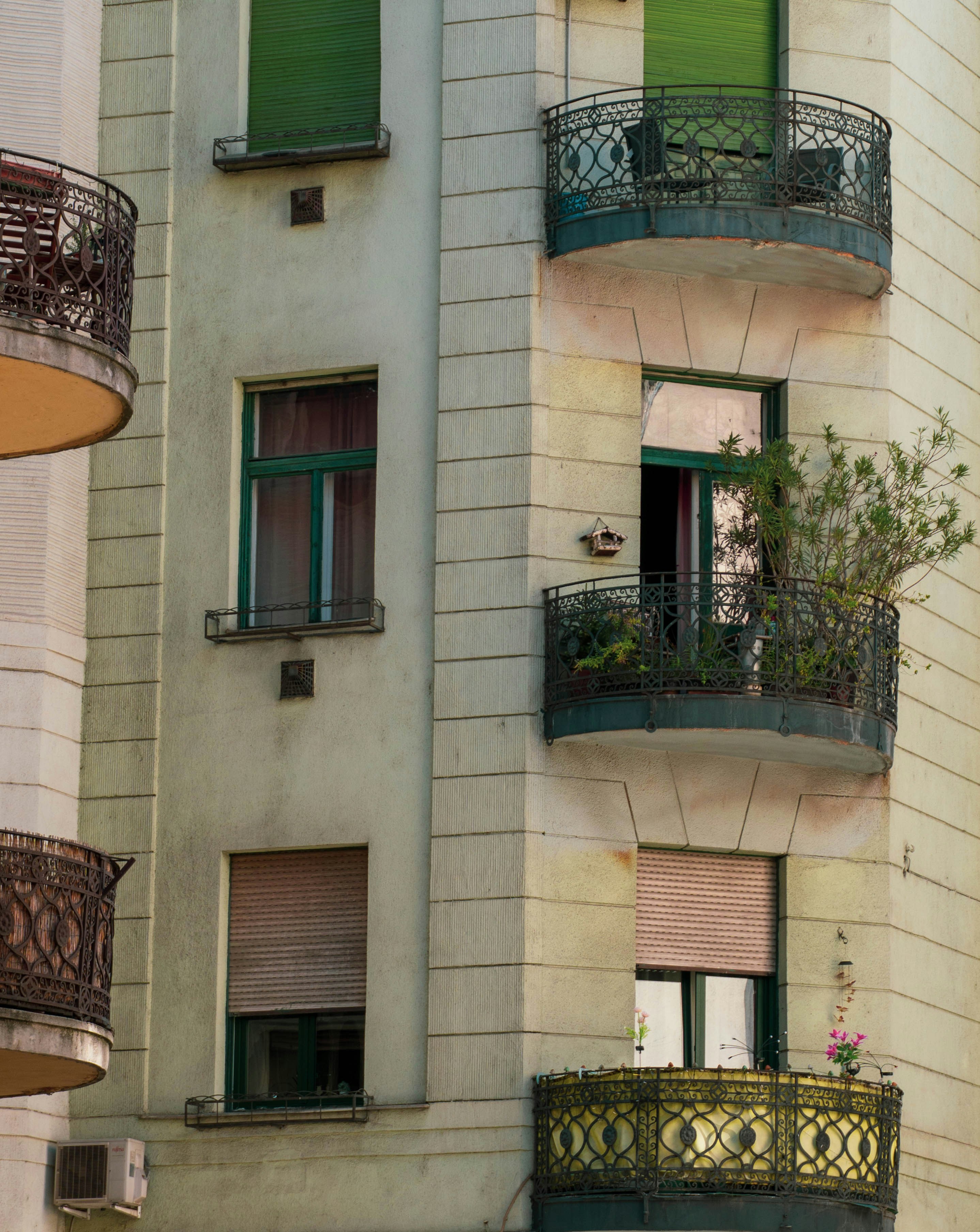 A corner of a building with wrought iron balconies and green window shutters