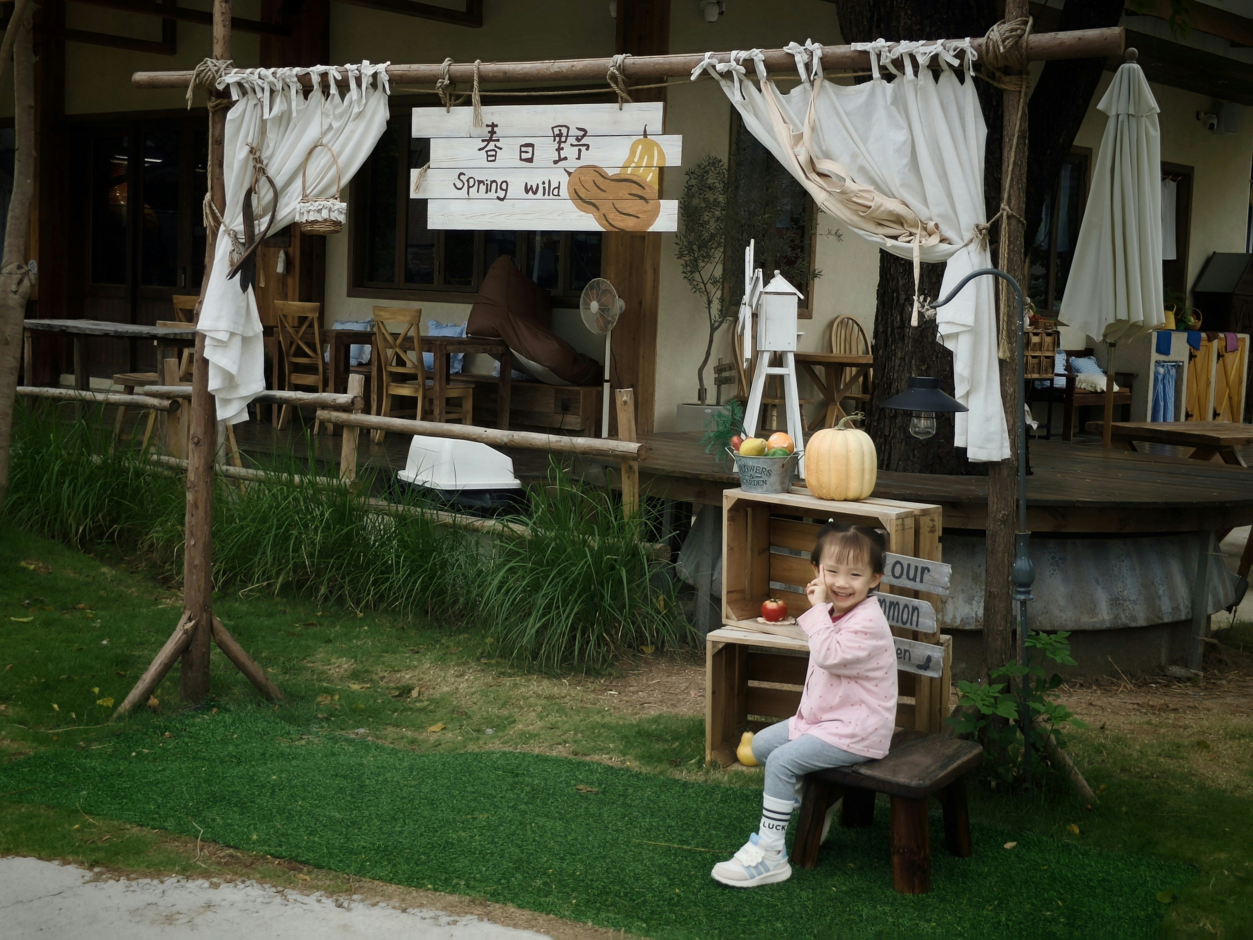 A smiling child sitting on a wooden stool in front of a rustic display