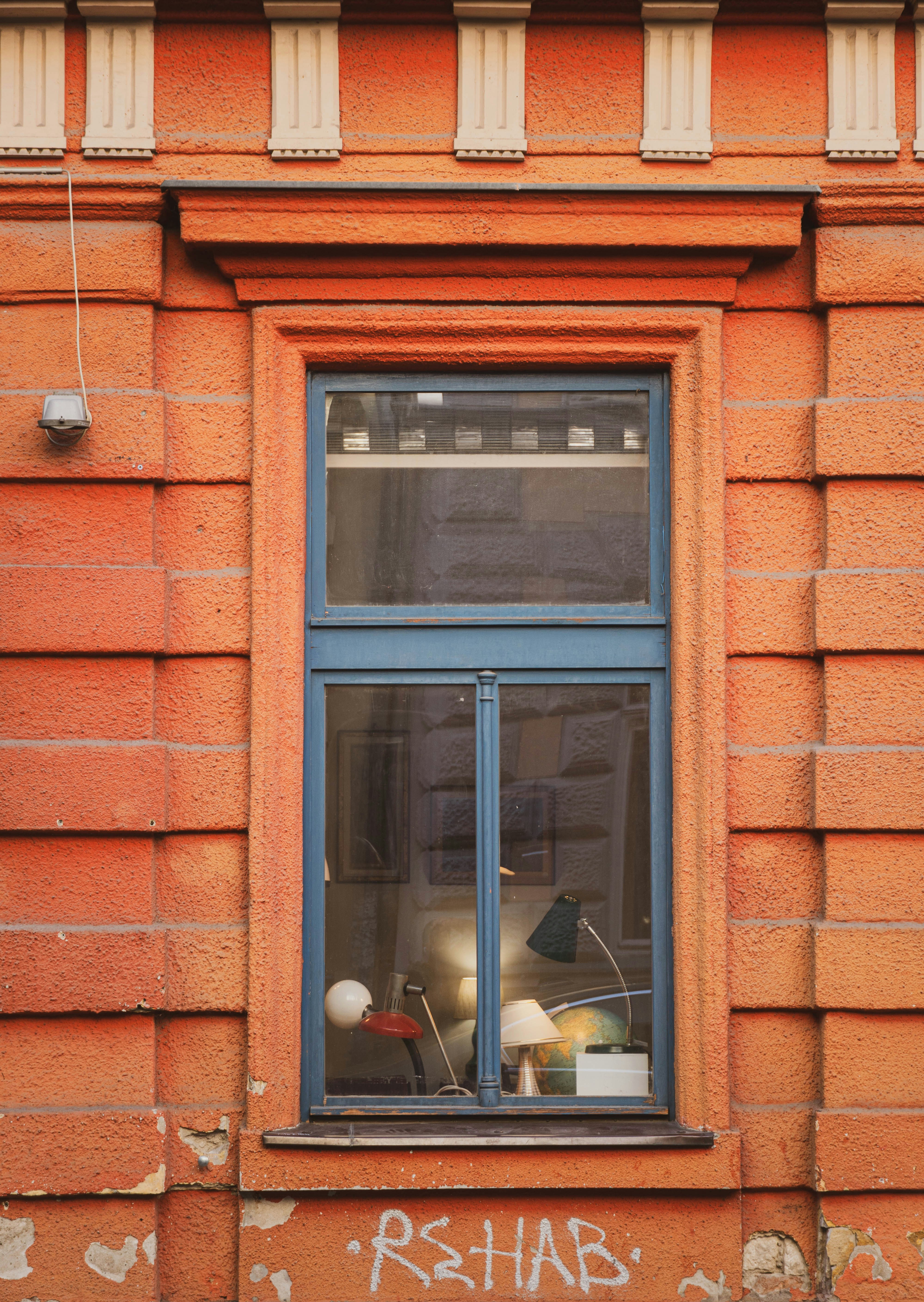 A blue window frame set into a textured orange brick wall with graffiti