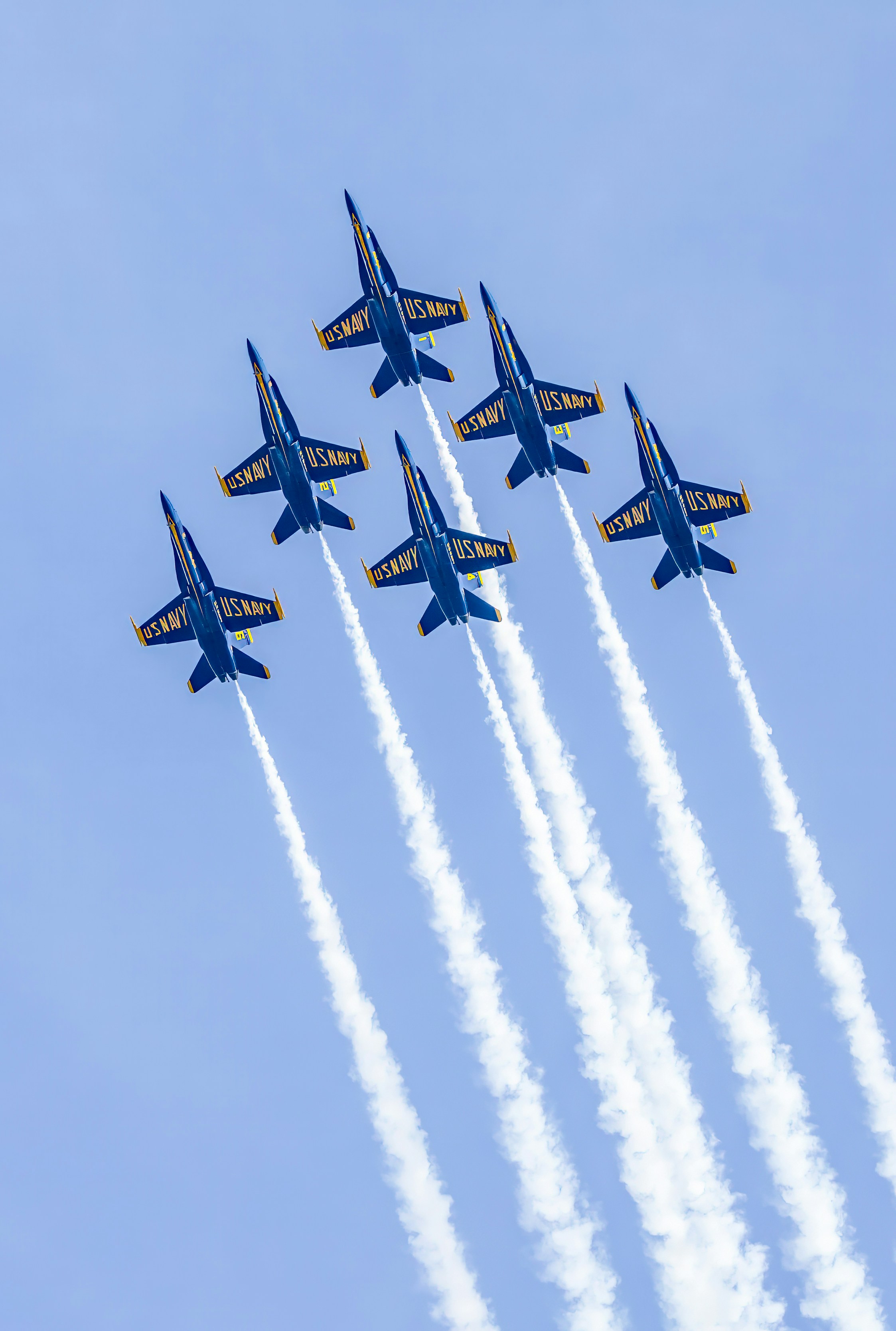 Five blue and yellow fighter jets flying in formation with white smoke trails