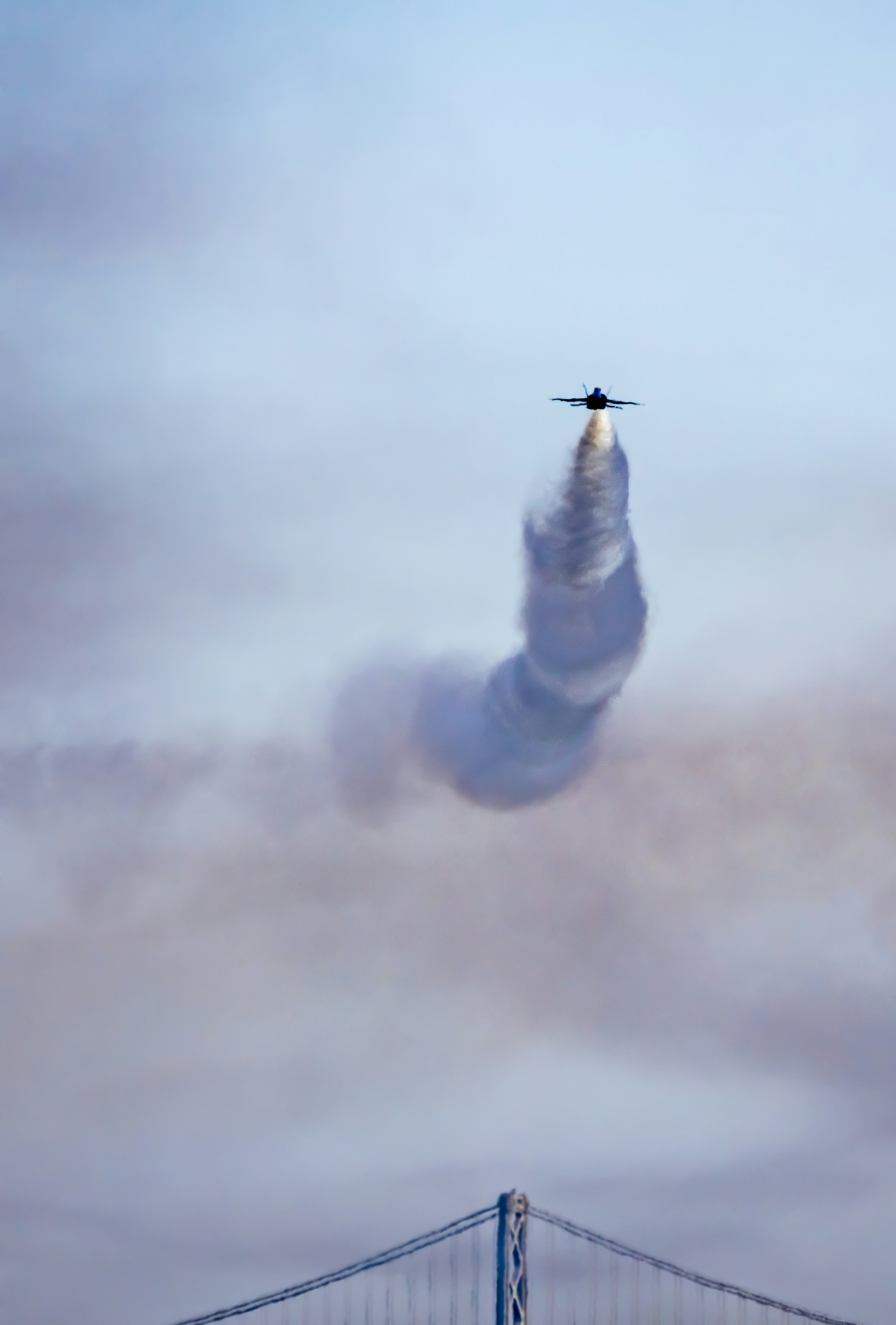 A jet trailing smoke above a suspension bridge under an overcast sky in San Francisco