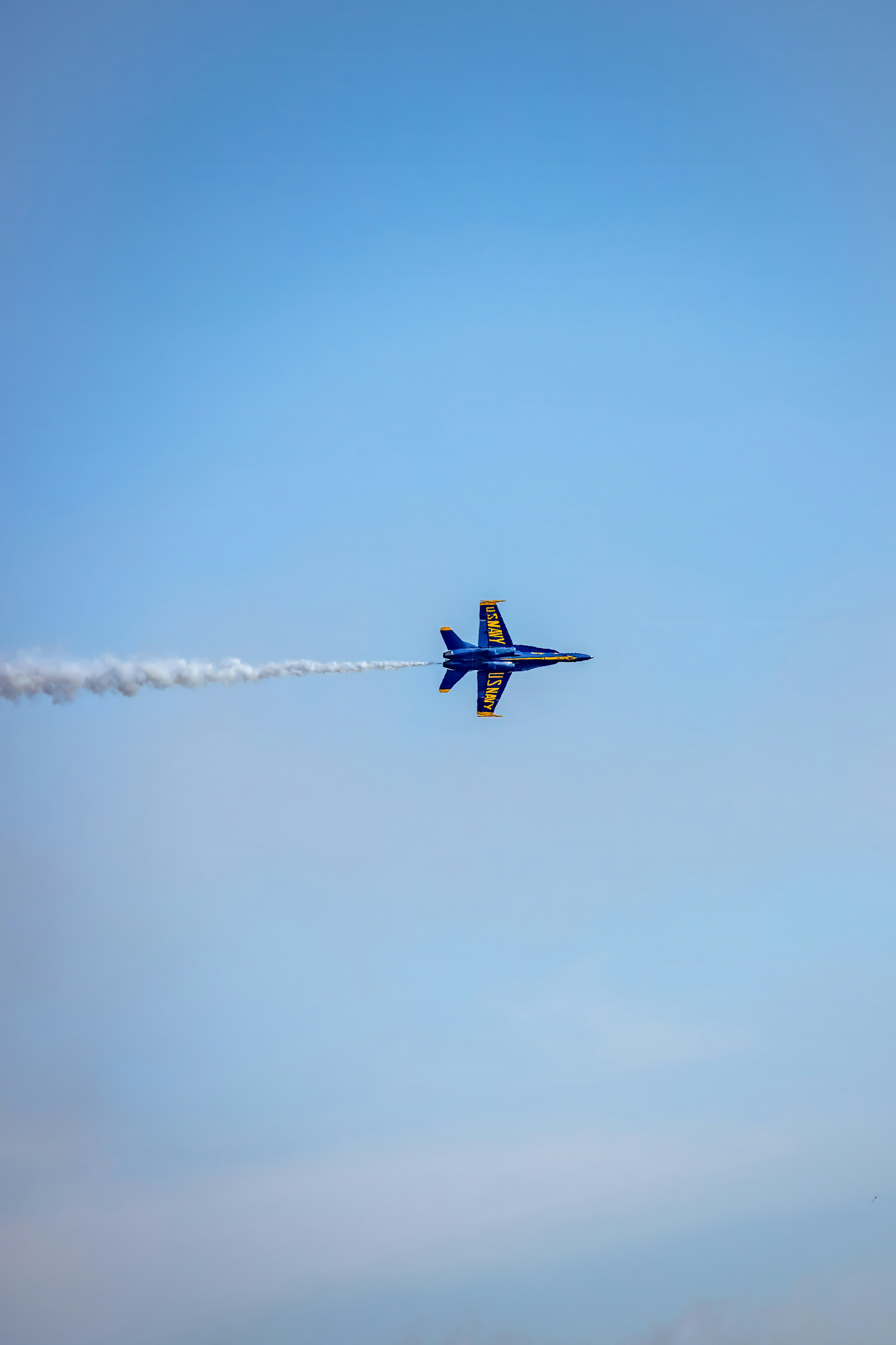 A blue and yellow fighter jet flying through a clear sky with smoke trails