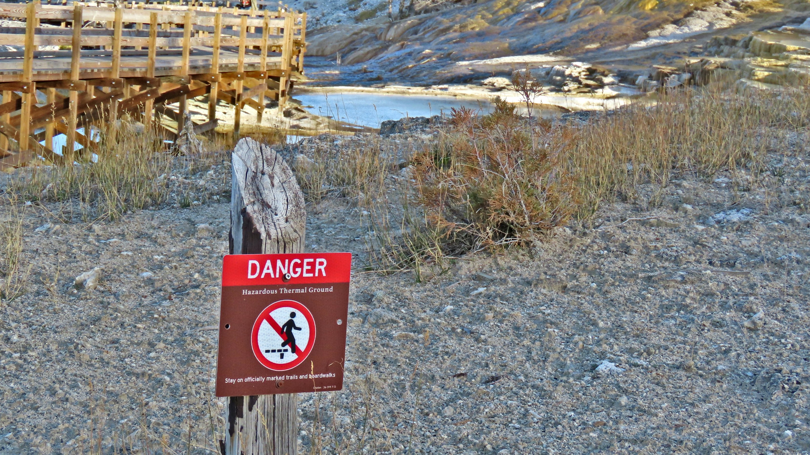 A danger sign on a wooden post near a thermal boardwalk and landscape