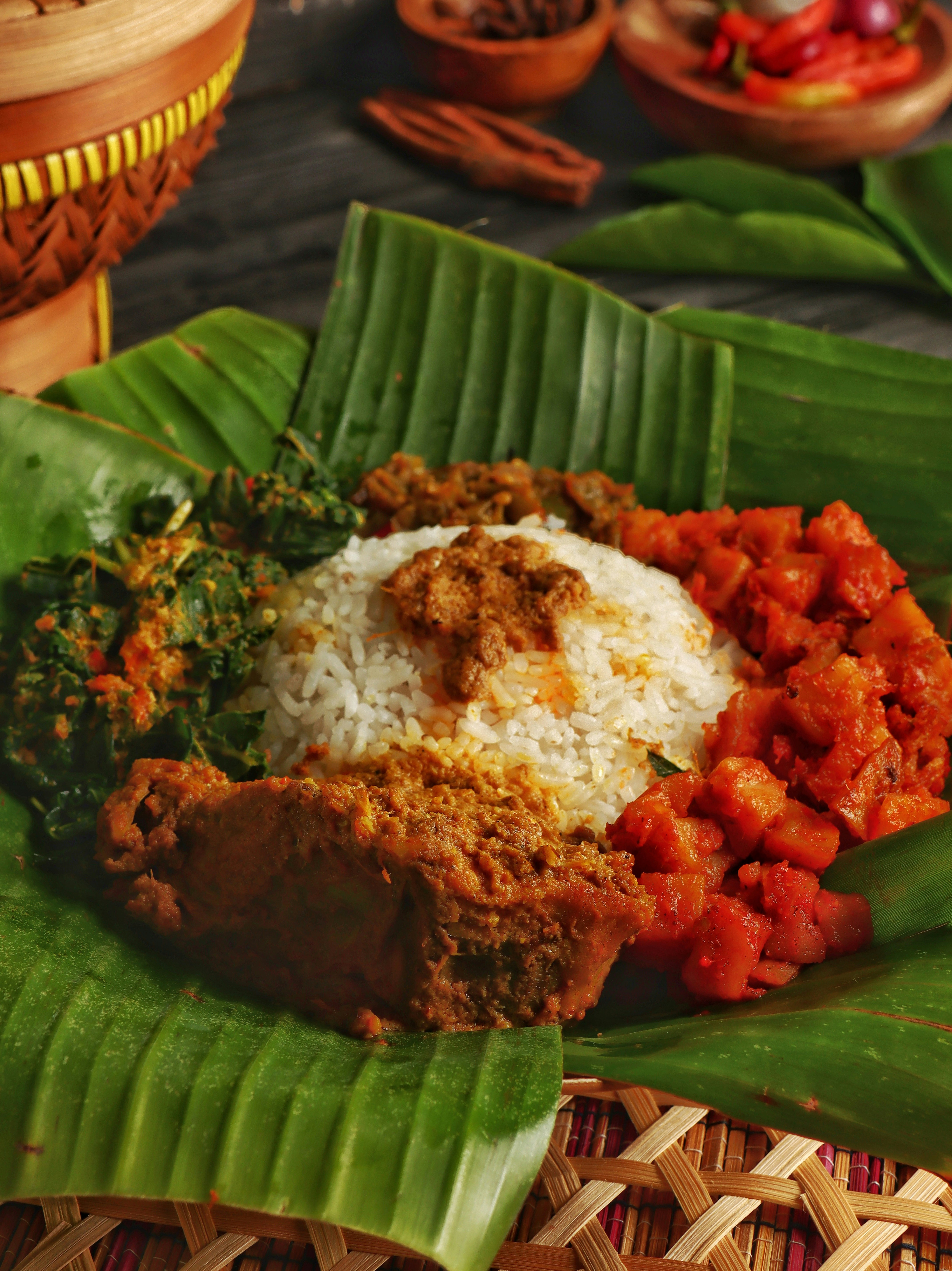 A mound of white rice served with spicy meat and vegetables on a banana leaf