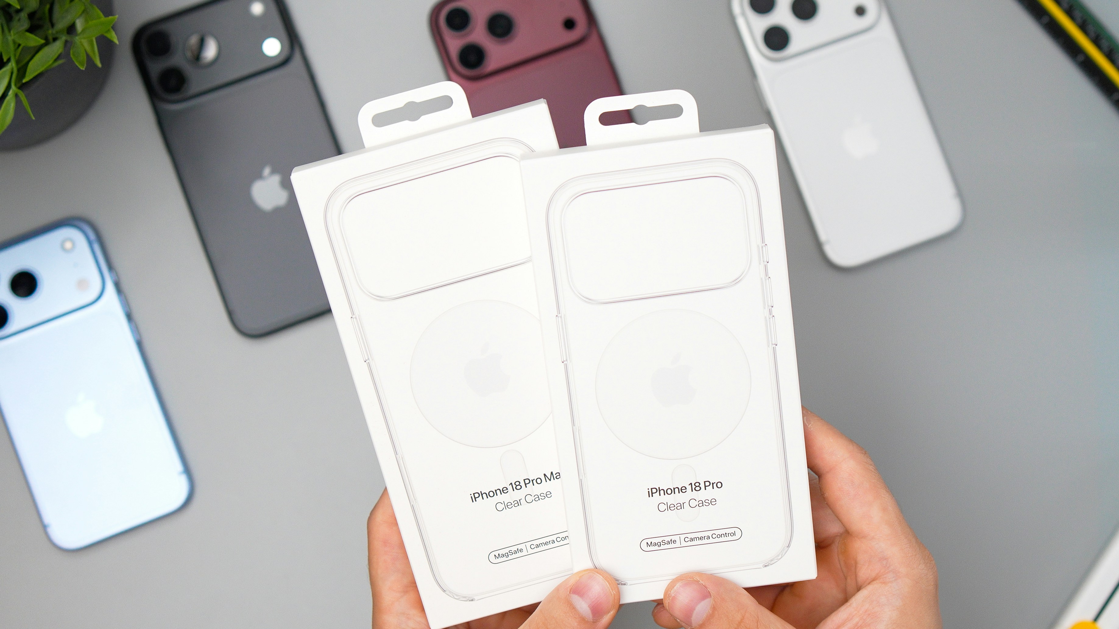 Two clear phone cases in white retail packaging held over a grey desk