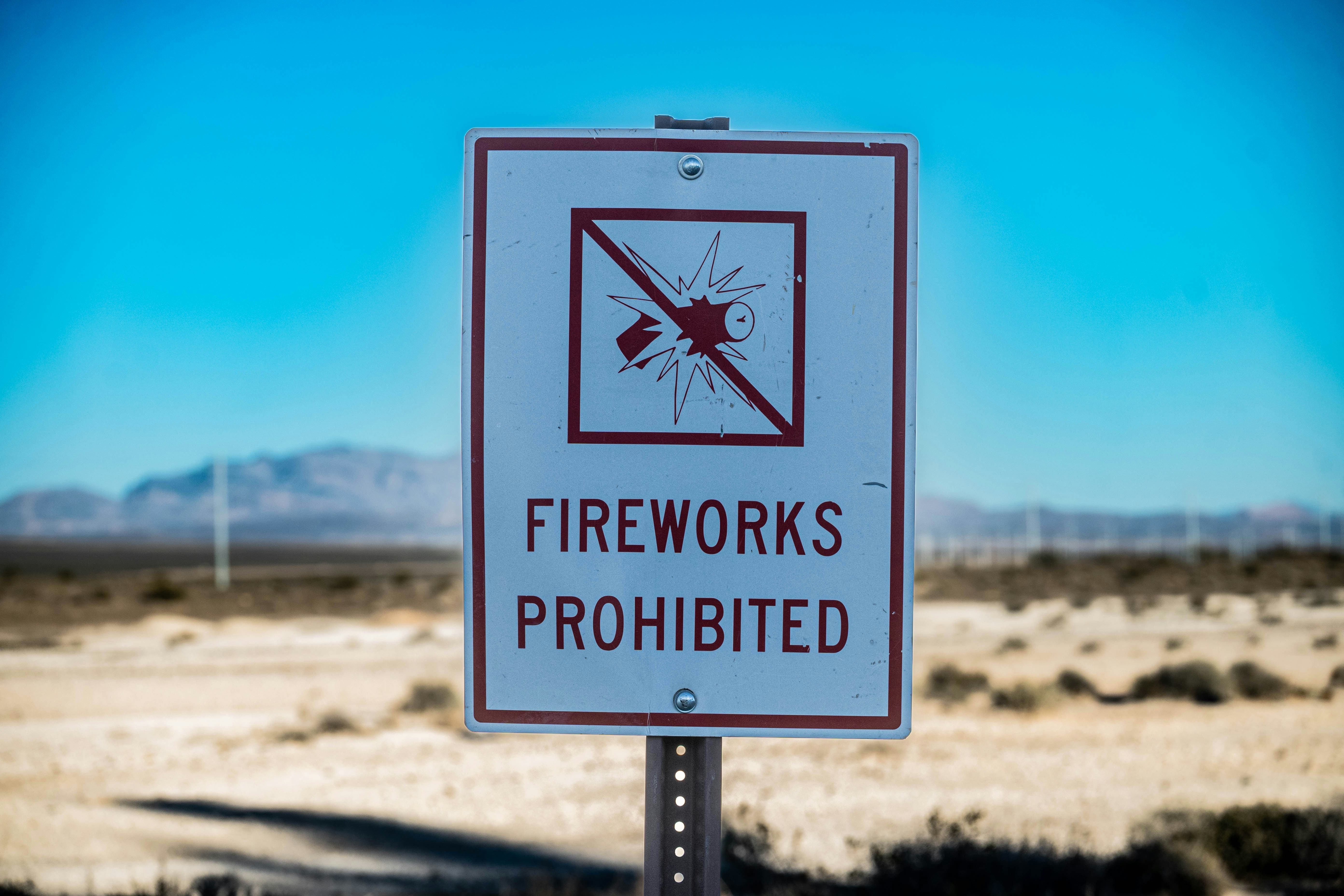 A sign reading "FIREWORKS PROHIBITED" with a graphic of an exploding firework in a desert