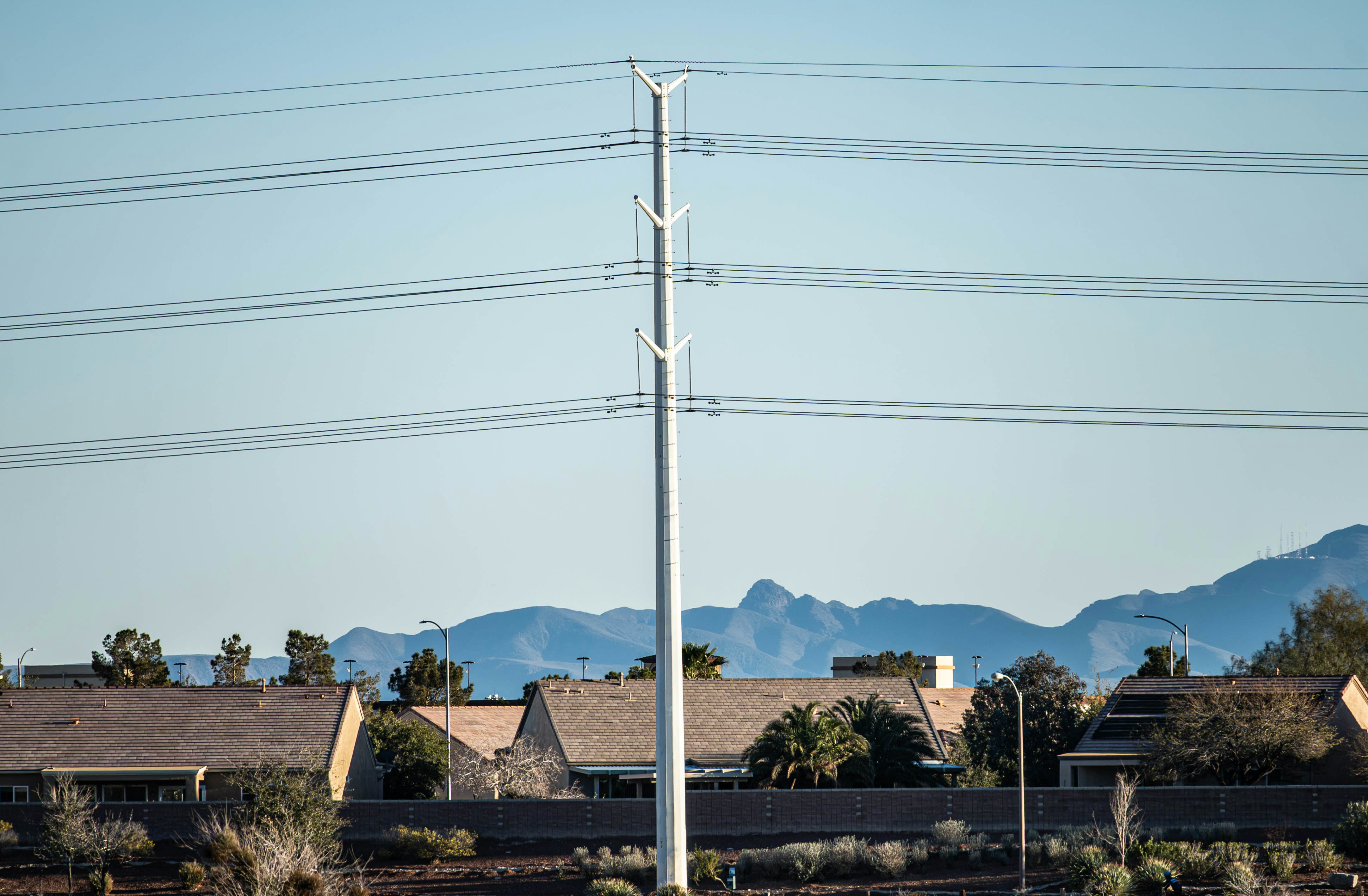 A tall white utility pole with power lines against a backdrop of distant mountains