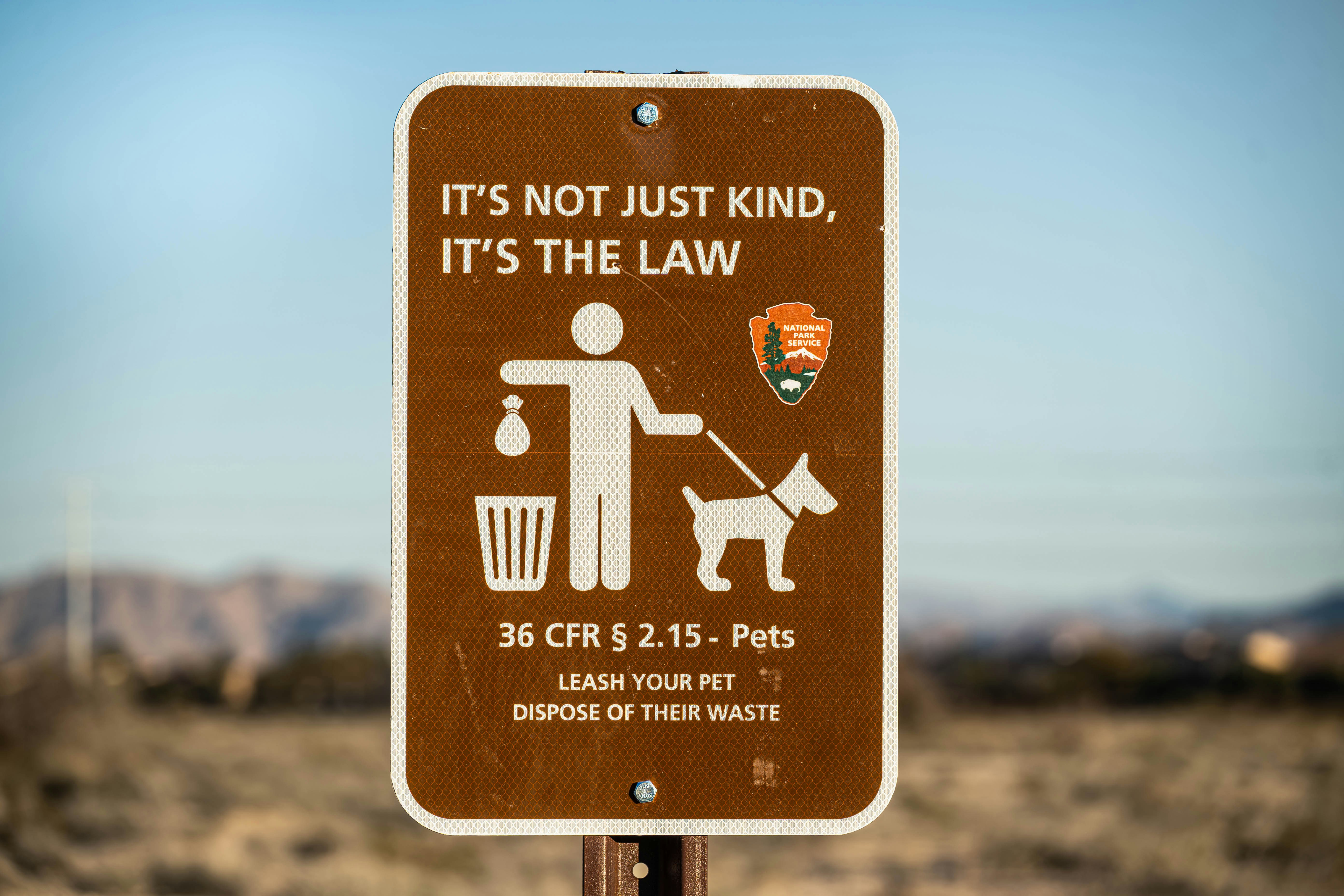 A brown National Park Service sign depicting a person with a dog and waste bag