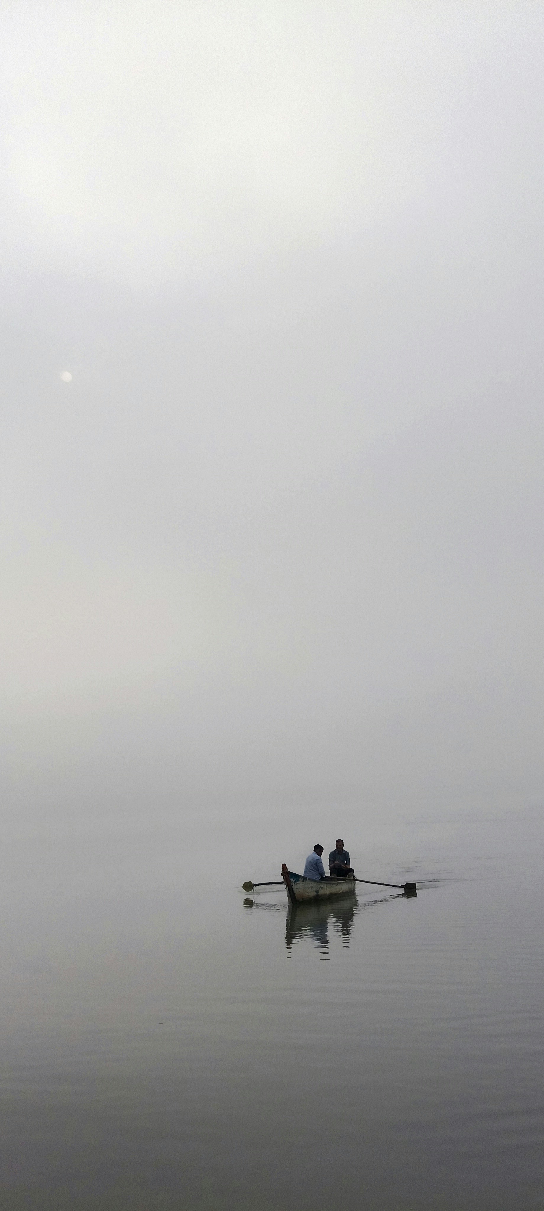 Duas pessoas remando em um pequeno barco de madeira em um lago calmo e enevoado
