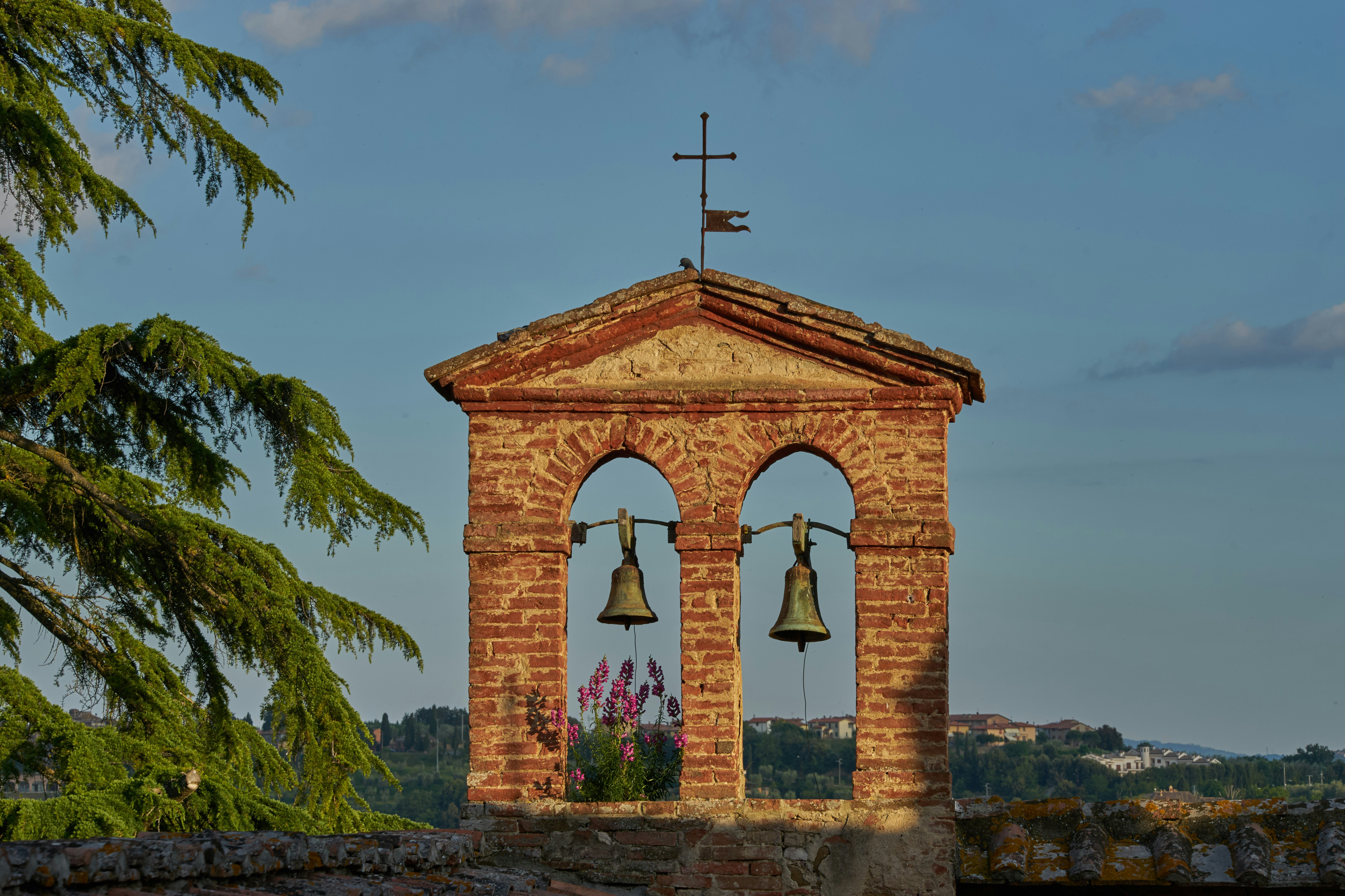 A brick bell tower with two bells and a cross against a blue sky
