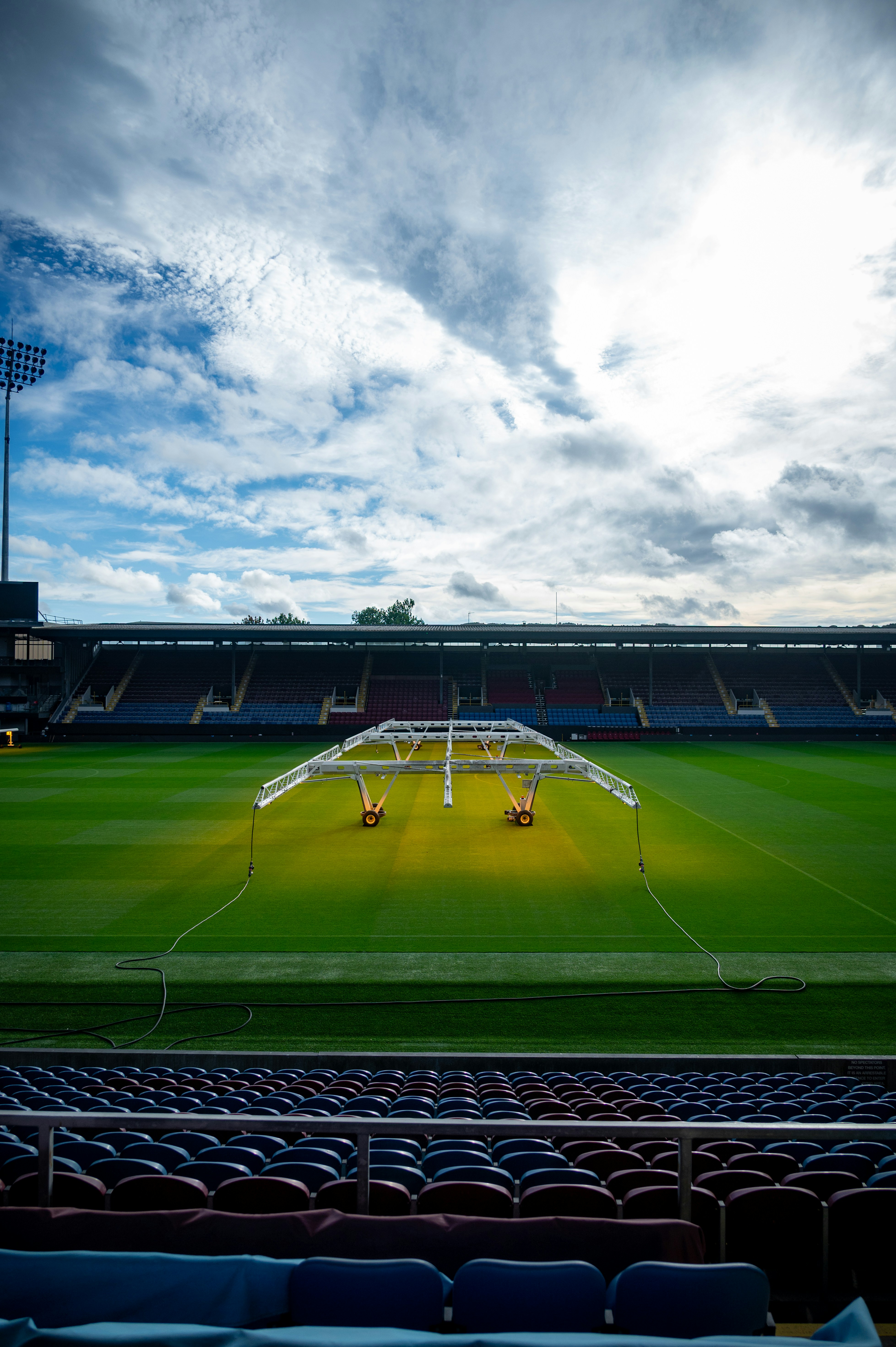 A mobile grow light rig over a green soccer pitch in an empty stadium
