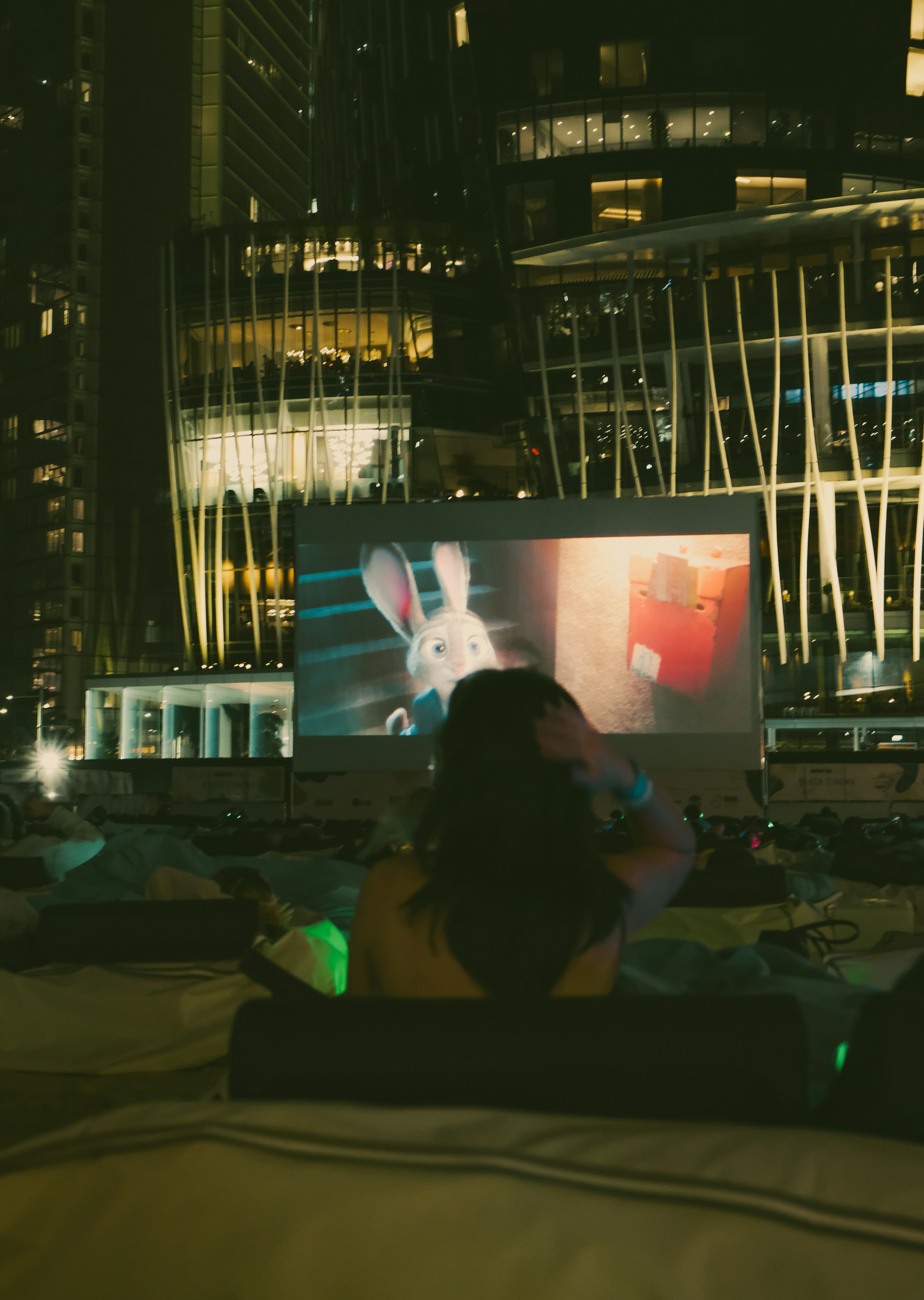 Una persona viendo una proyección de película al aire libre por la noche frente a edificios modernos