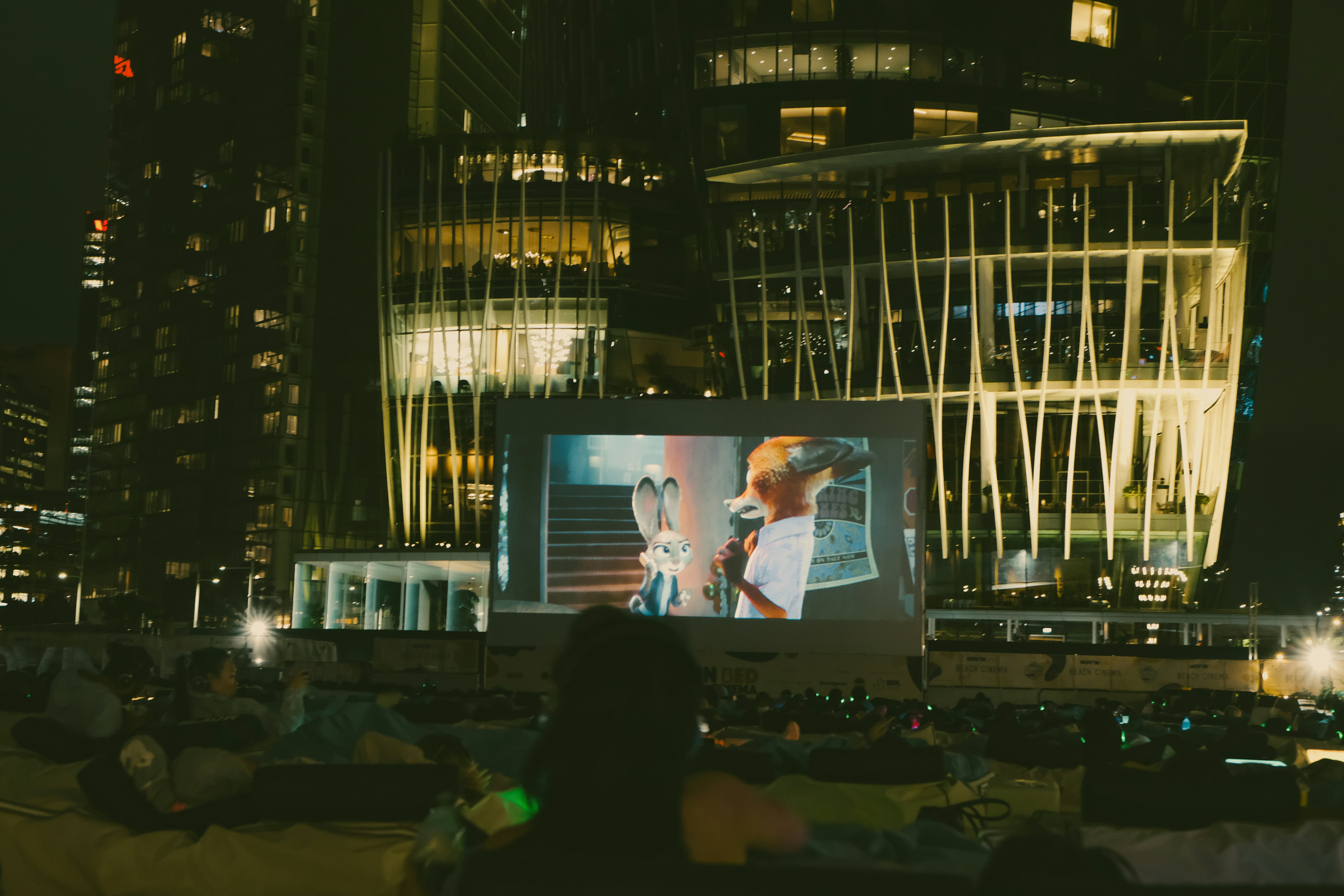 Una proyección en un cine al aire libre con una película de animación proyectada ante un moderno edificio de cristal