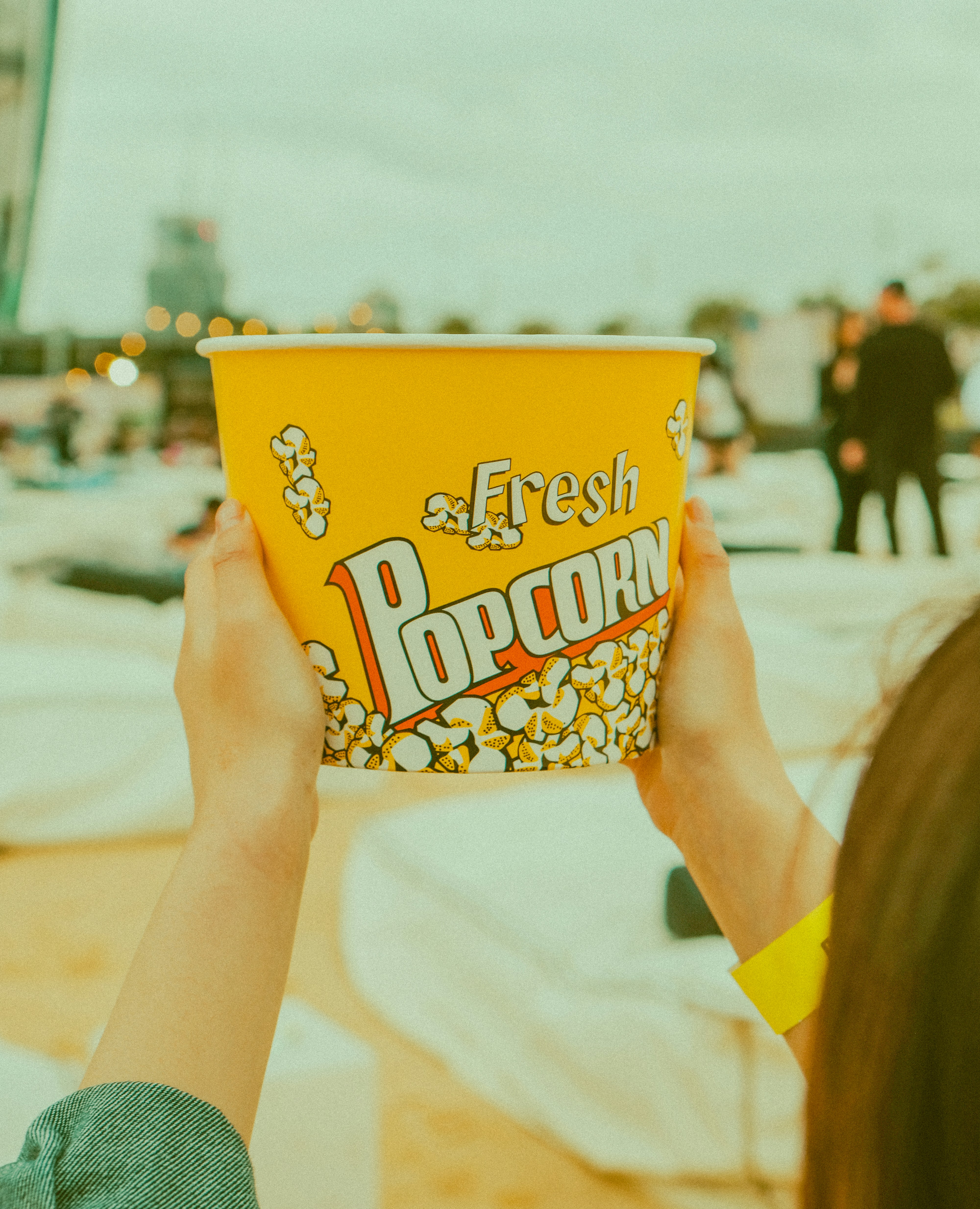 Una persona sosteniendo un cubo amarillo de palomitas en un evento al aire libre