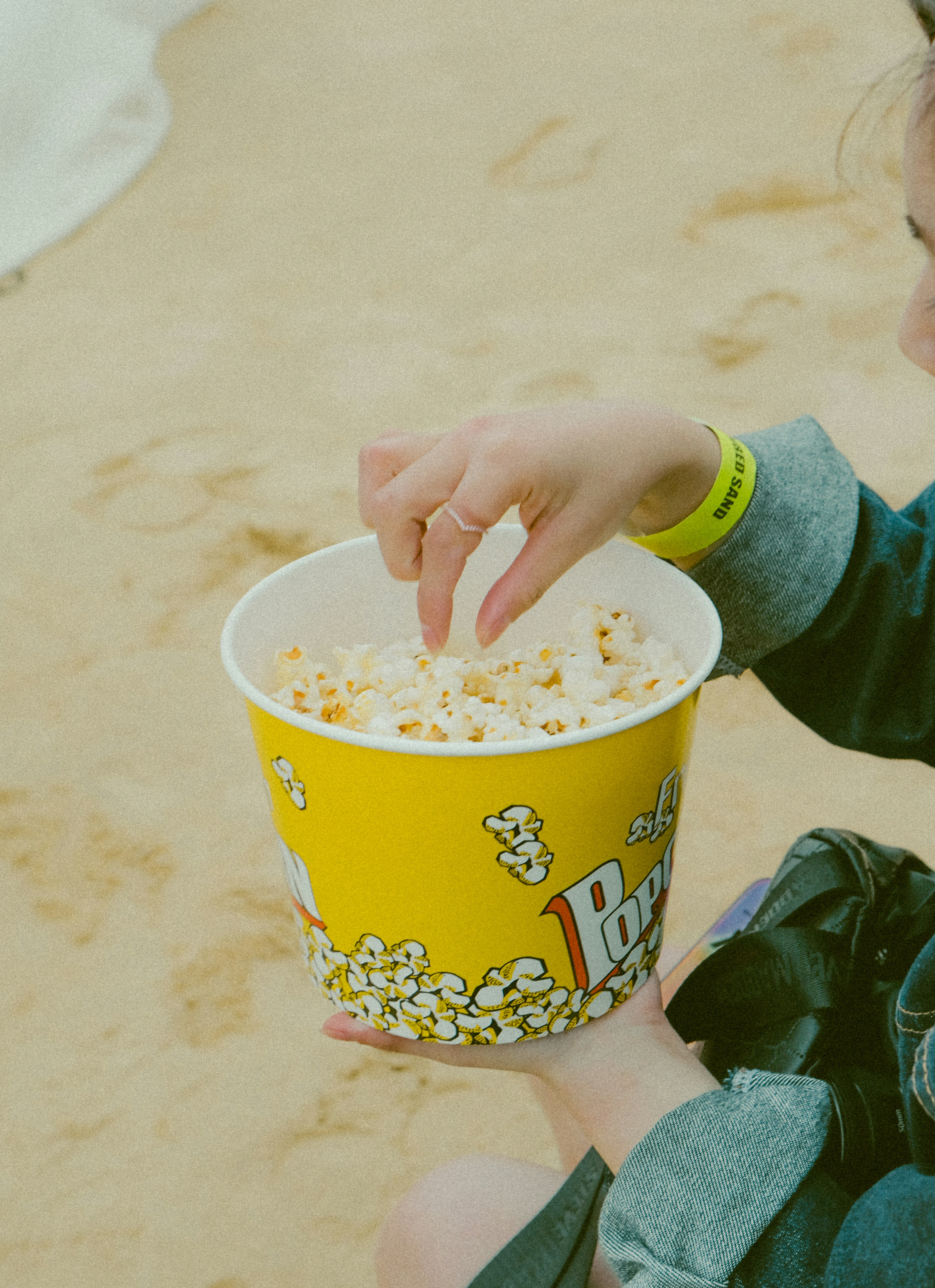 Una persona metiendo la mano en un cubo amarillo de palomitas en una playa de arena