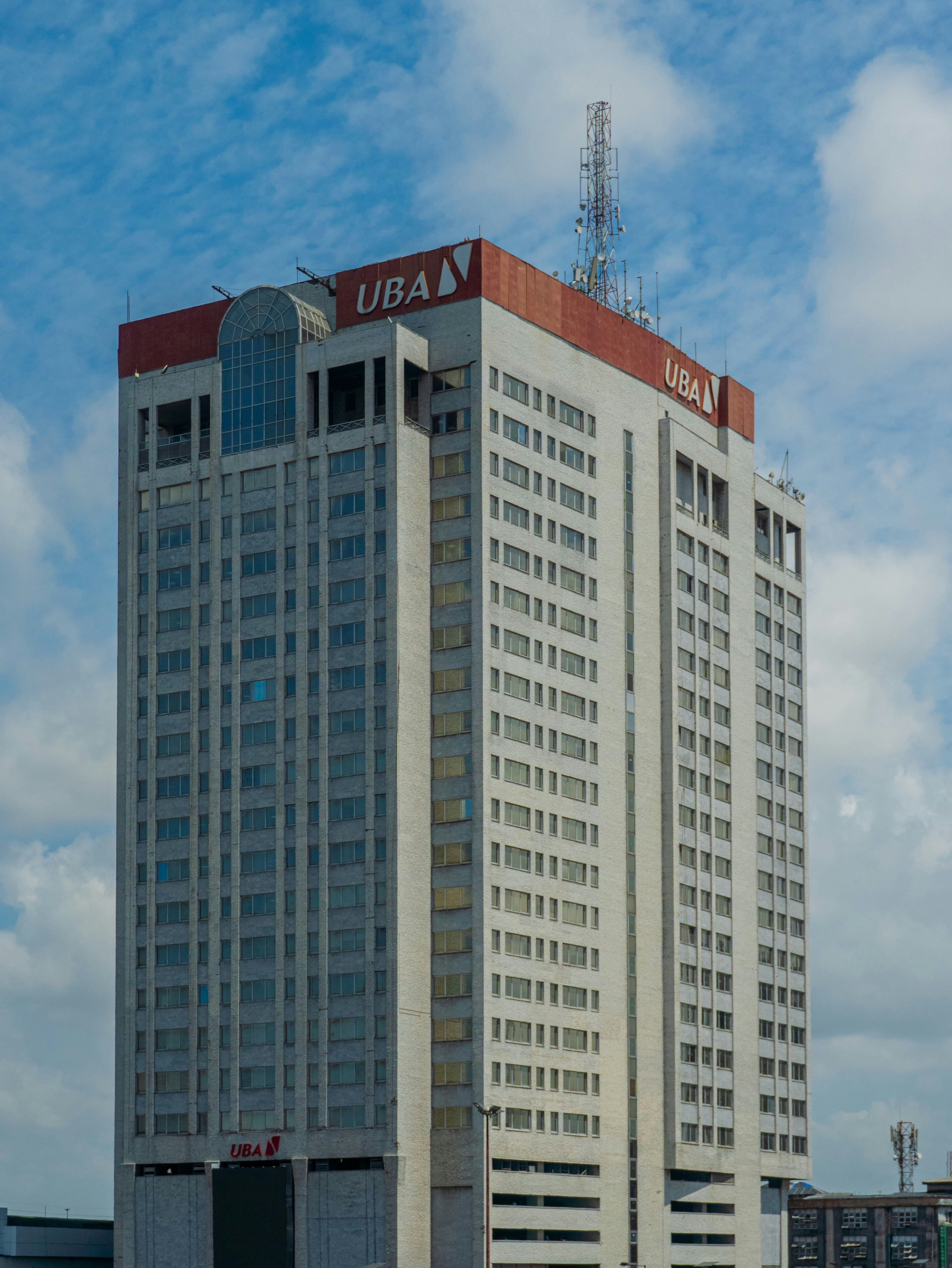 A tall skyscraper with UBA signage against a blue sky with white clouds
