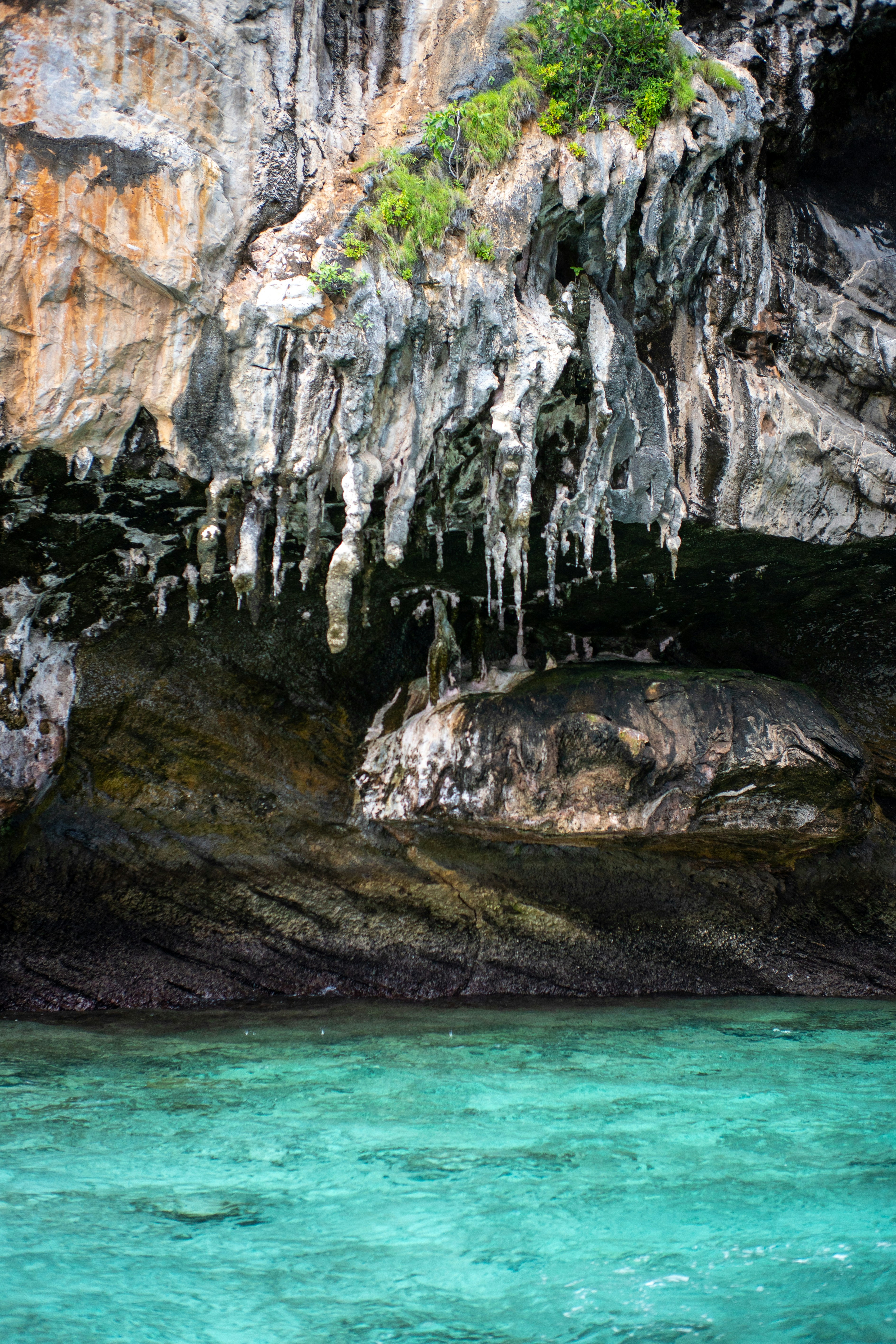 Stalactites hanging from a rocky limestone cliff above clear turquoise water