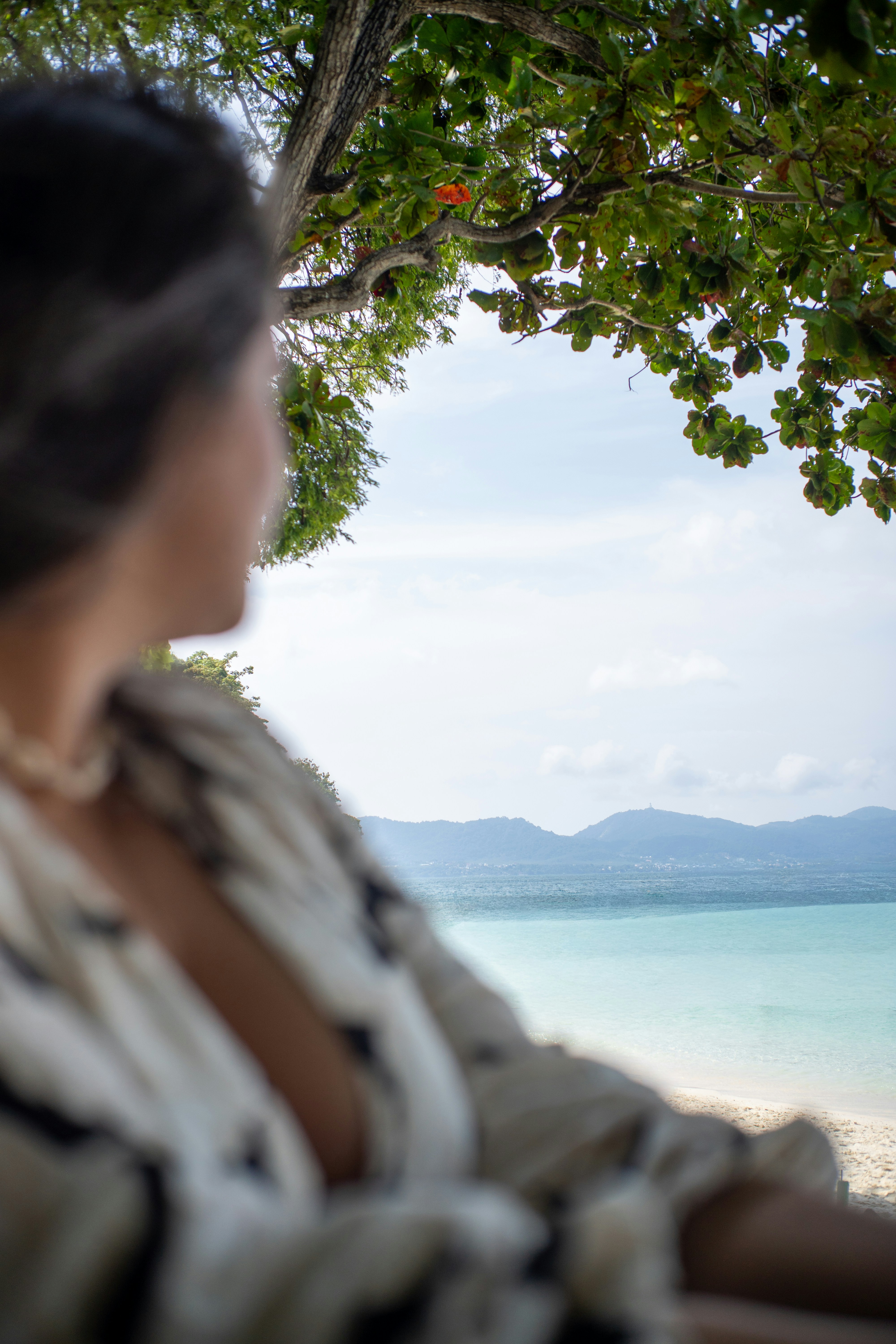 A person in a patterned shirt looking out at a tropical beach and mountains