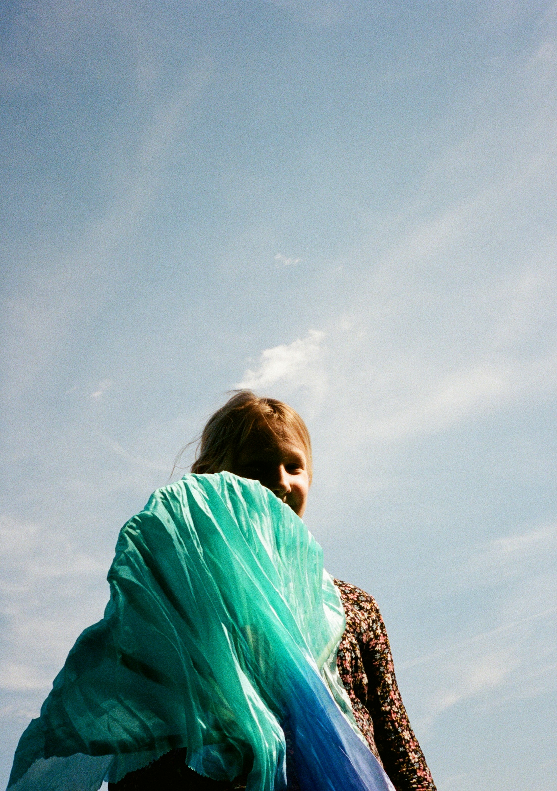 A person holding a bright teal fabric against a clear blue sky