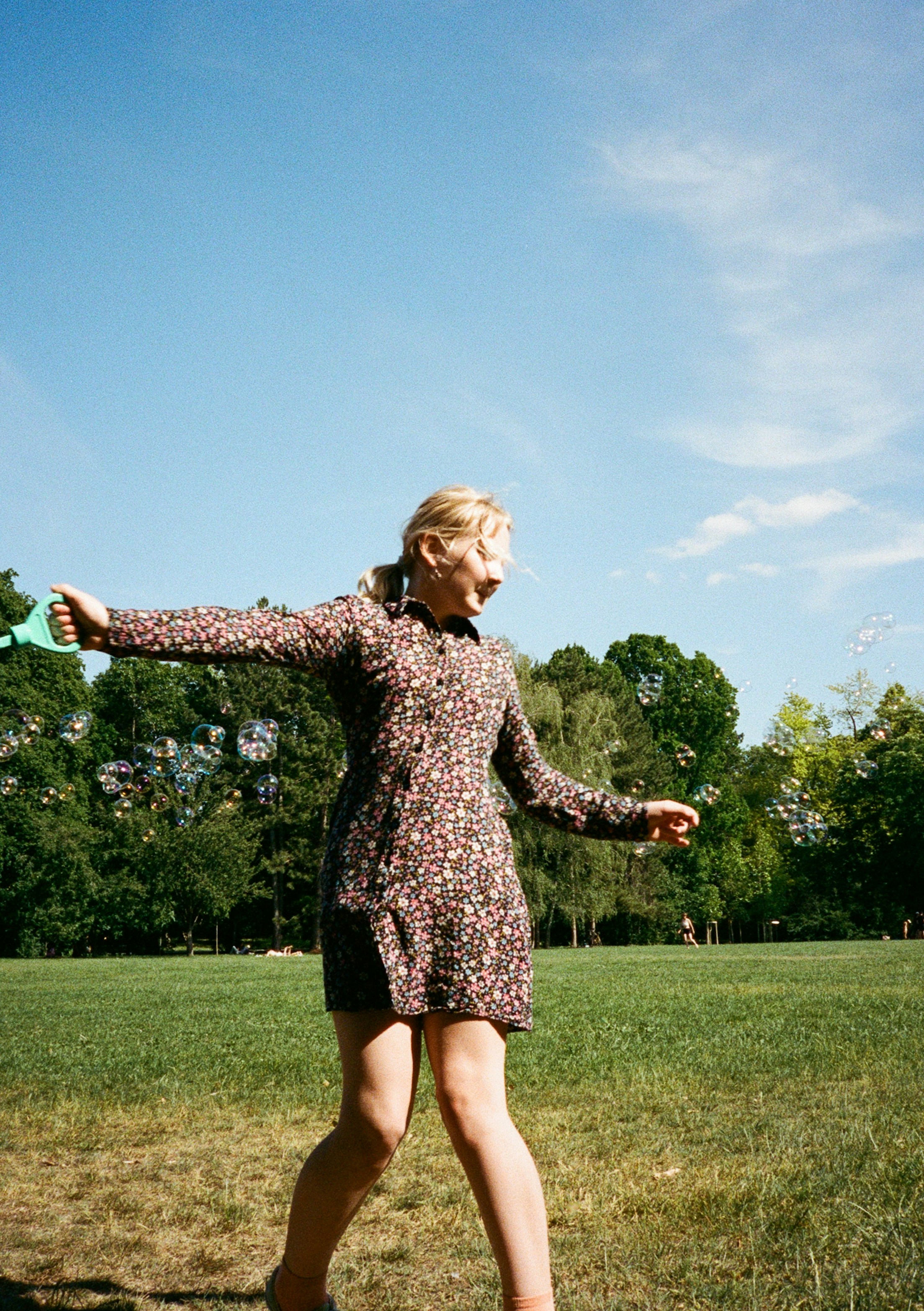 A girl in a floral dress making bubbles in a park in Budapest