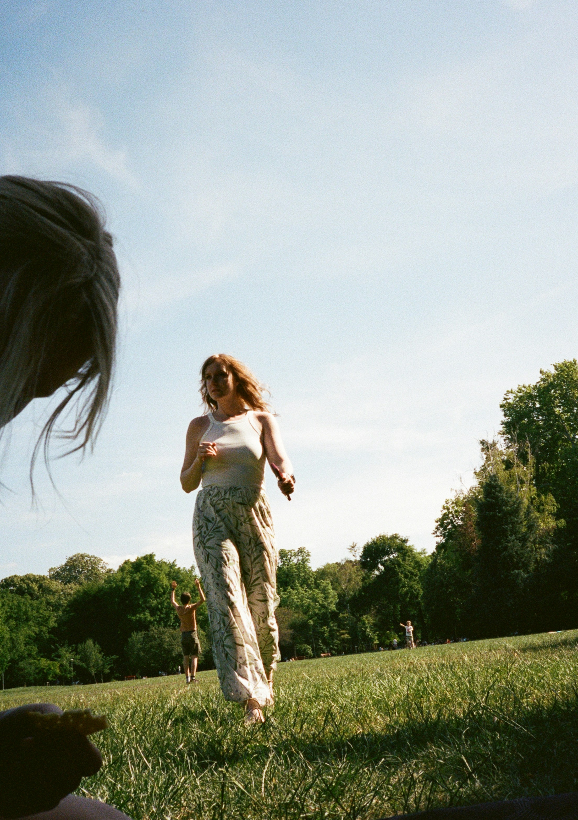 A woman in a white tank top and patterned trousers walking through a park