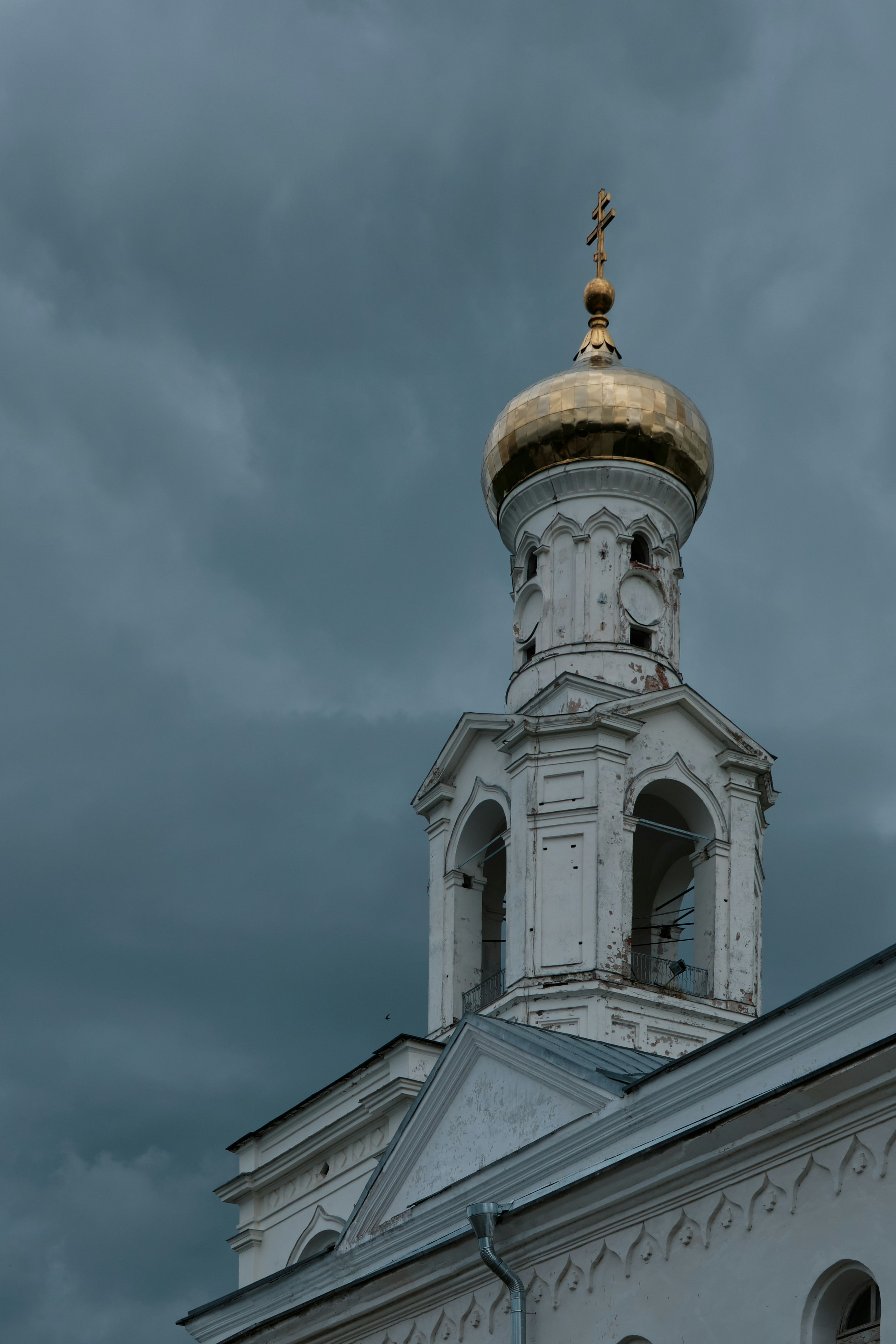 A white church tower with a golden dome against a dark stormy sky