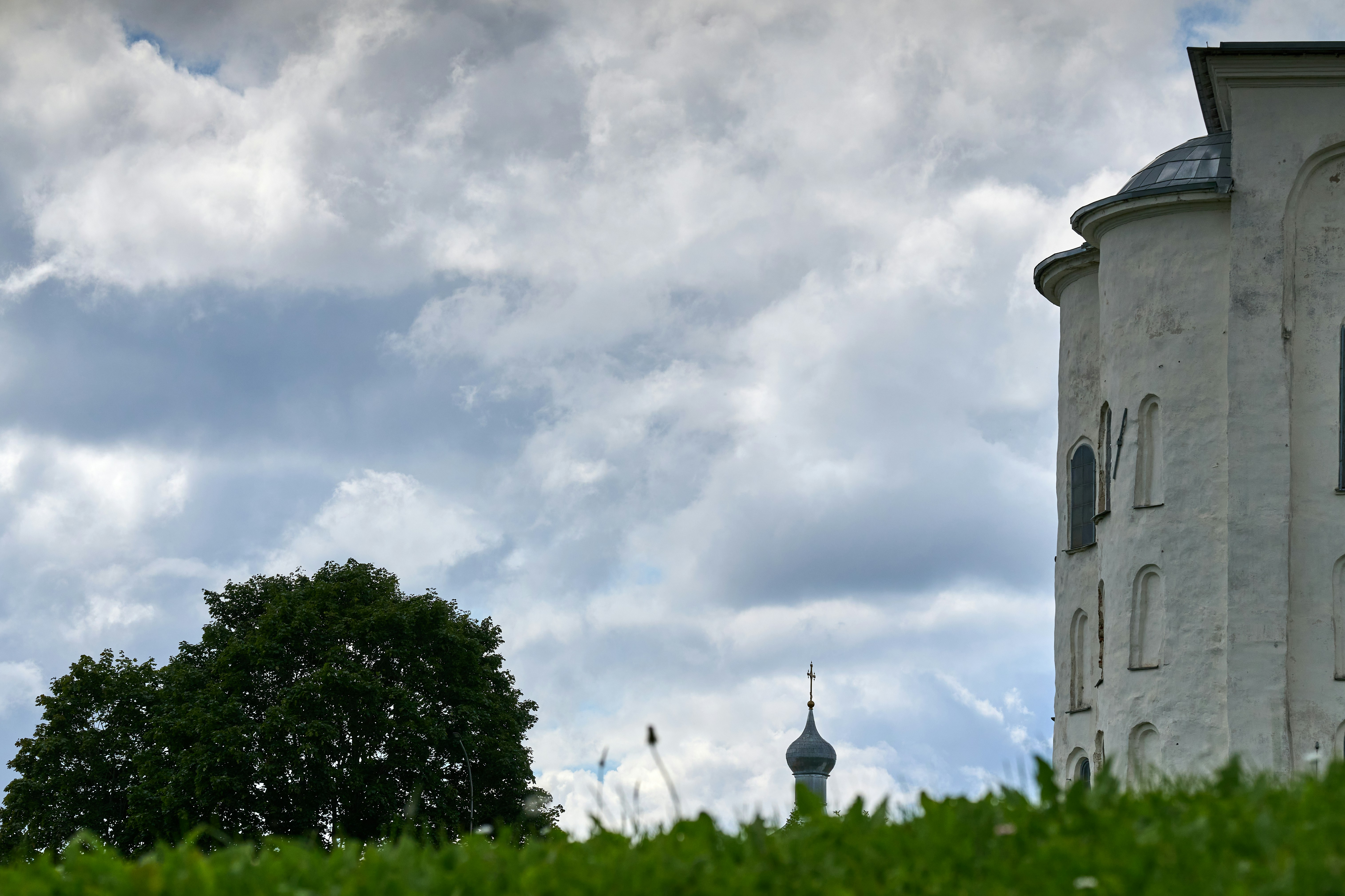A white stone church wall and a distant onion dome under a cloudy sky