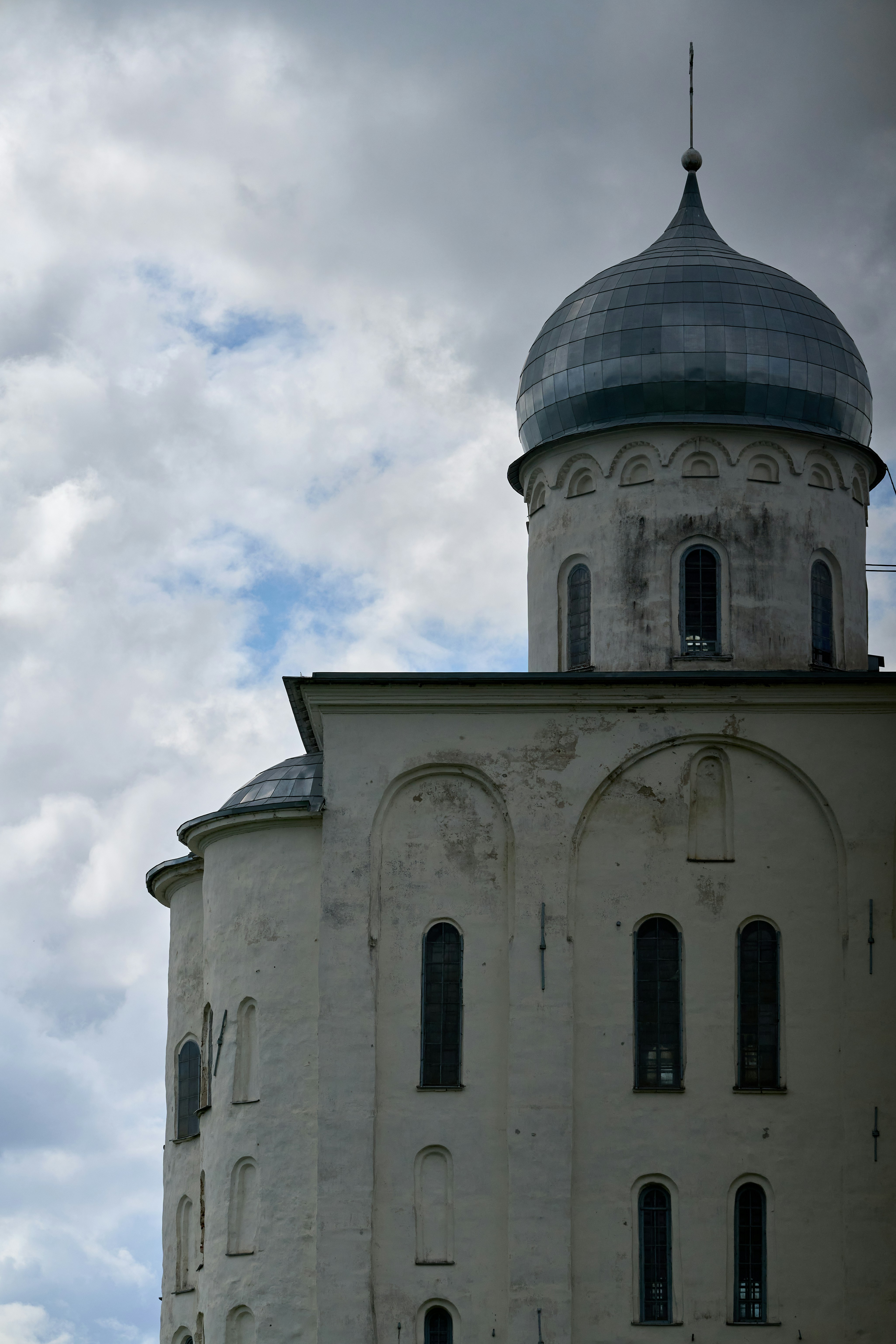 A white stone church with a grey metal dome under a cloudy sky